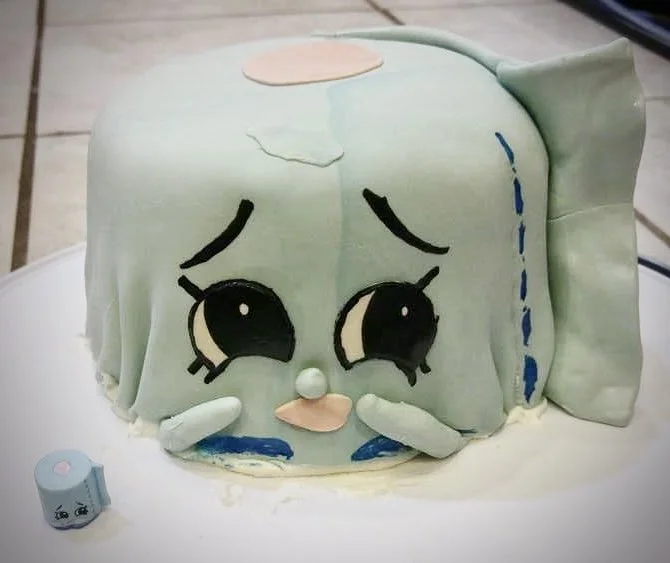 A cake decorated to look like a tired, sad fish with large anime-style eyes, lying on a white surface.