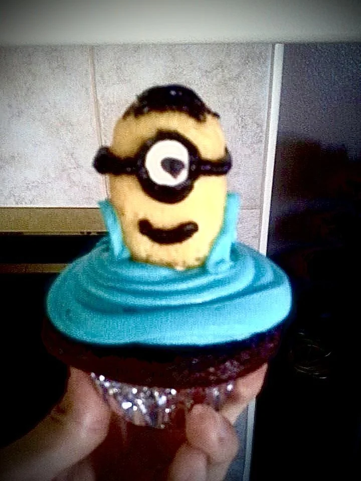 Cupcake decorated with a Minion face made from frosting, with yellow, blue, and black icing for details.
