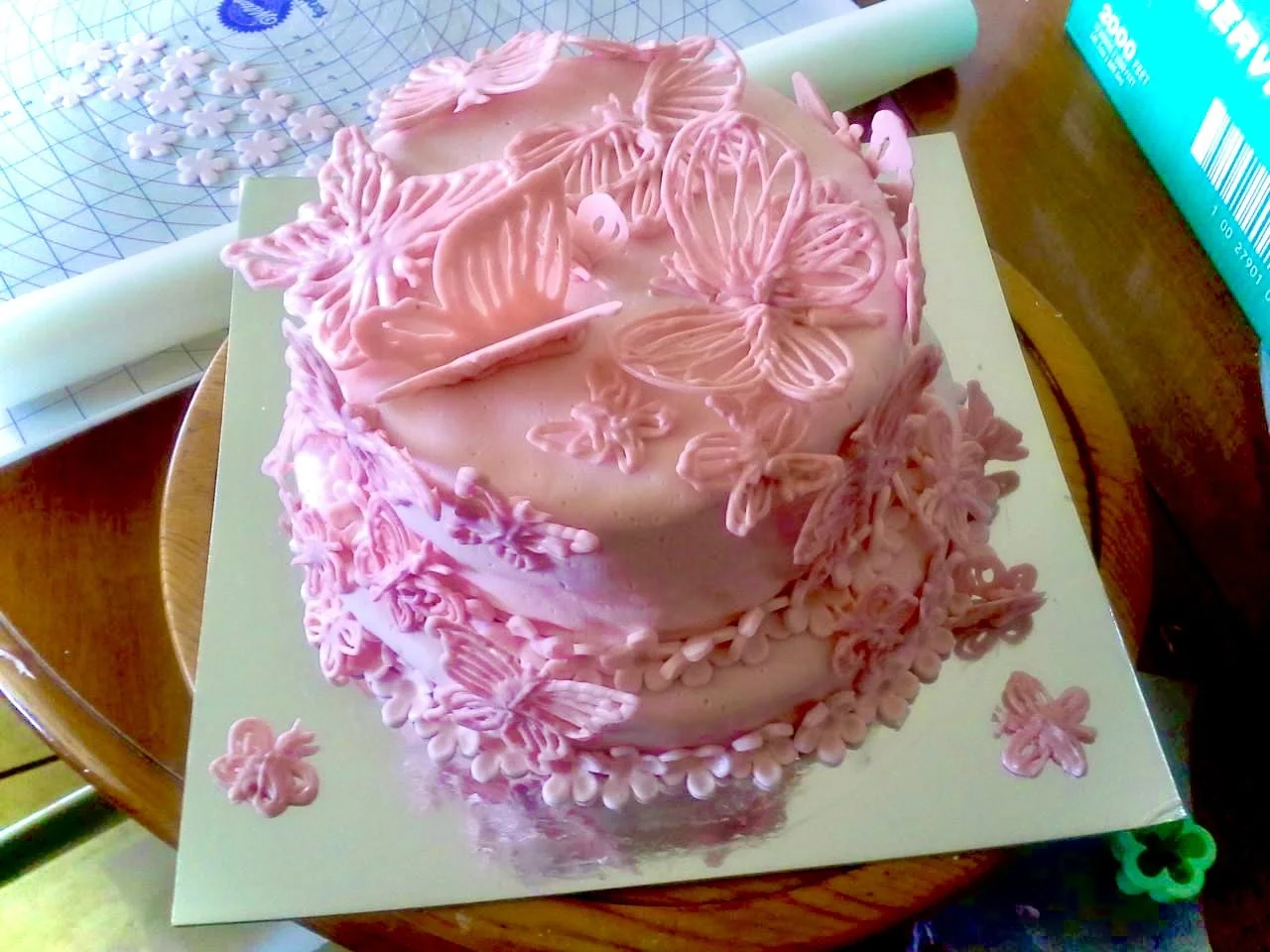 Pink frosted birthday cake decorated with pink butterfly and flower toppers on a white cake board.