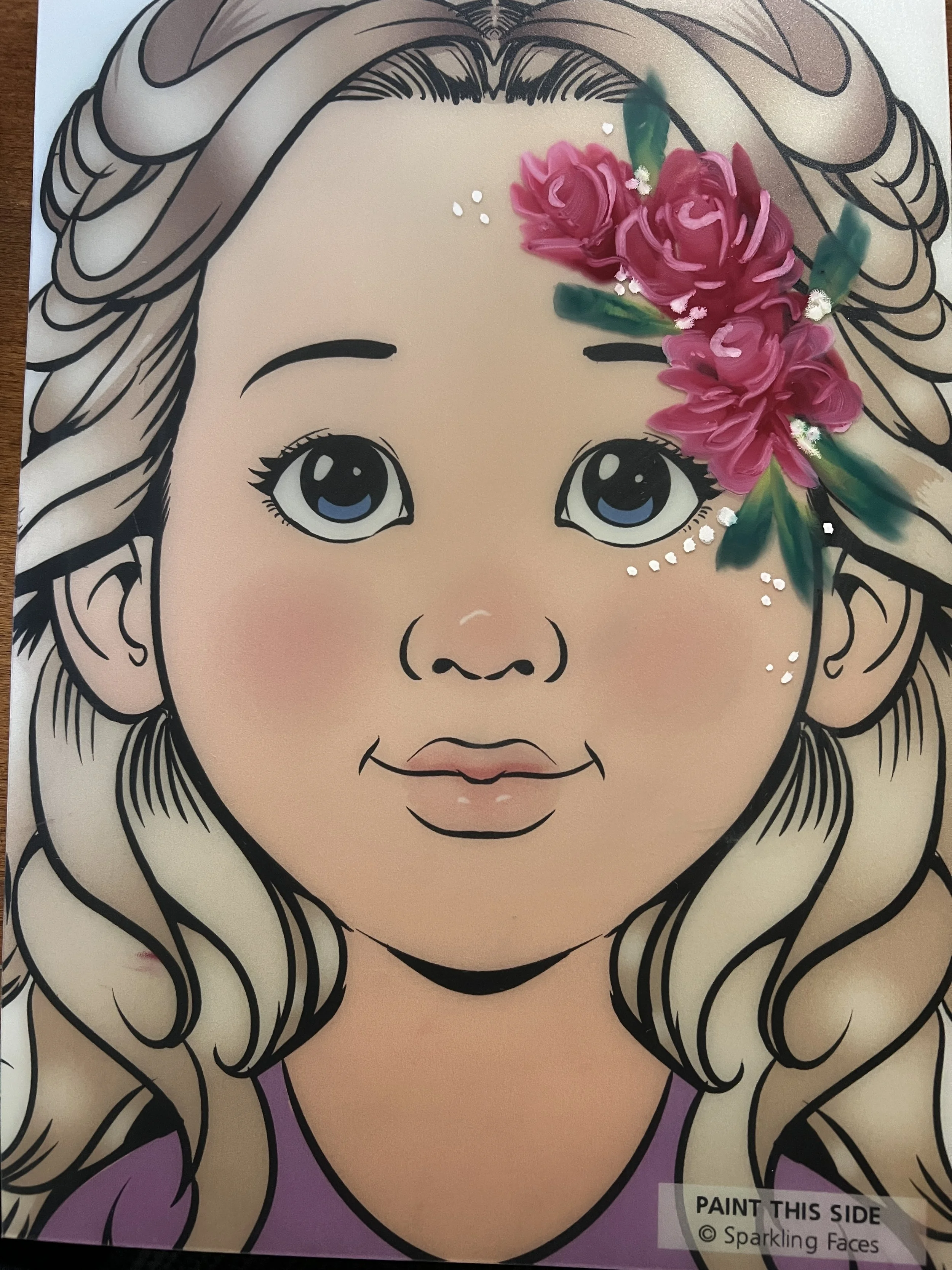 A coloring poster of a young girl with blonde wavy hair, large eyes, and pink lips, decorated with a 3D pink flower and green leaves on the right side of her hair.
