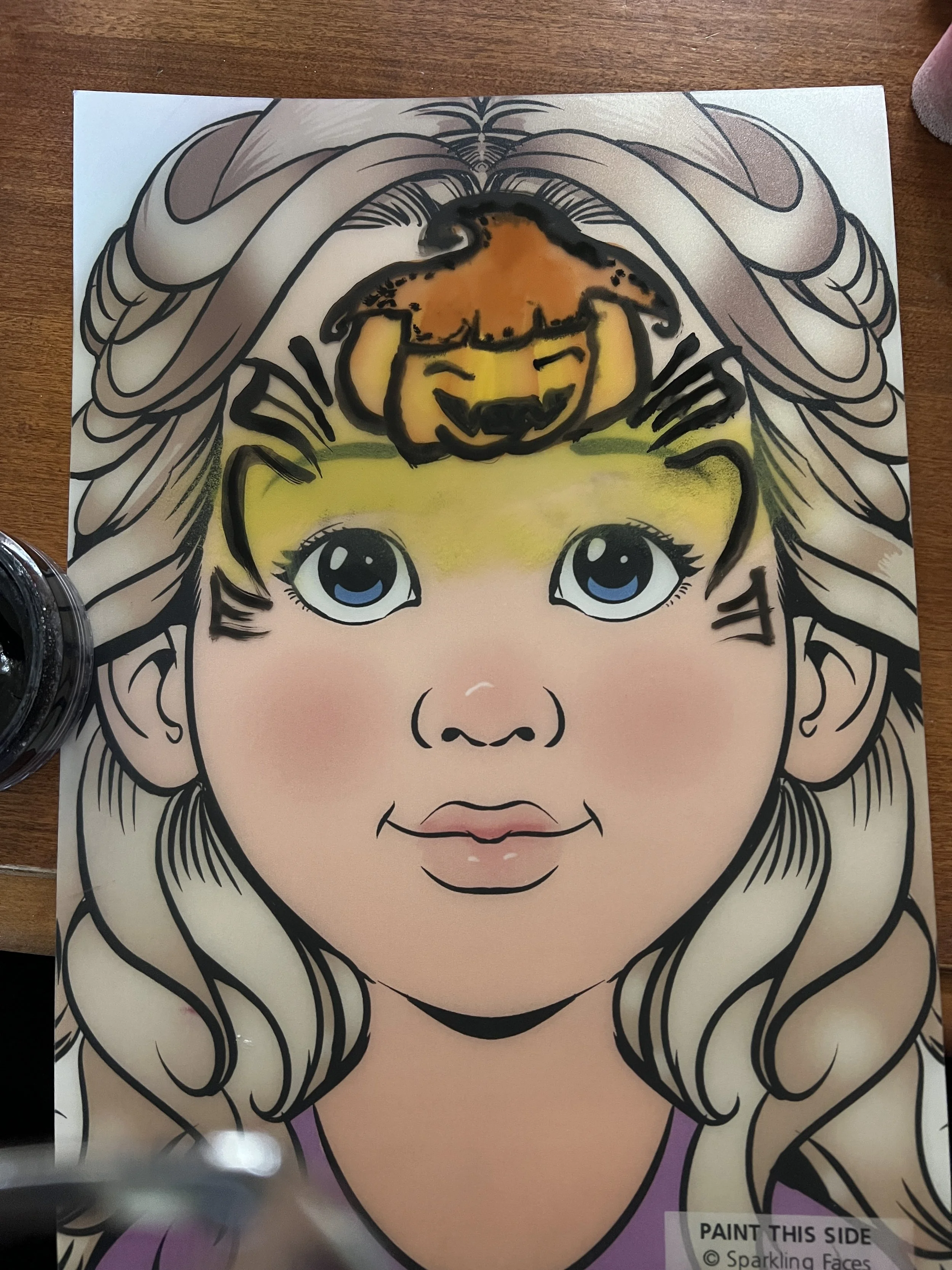 A coloring page drawing of a young girl with large blue eyes, long wavy hair, and a henna tattoo on her forehead, with a small dog sitting on her head.