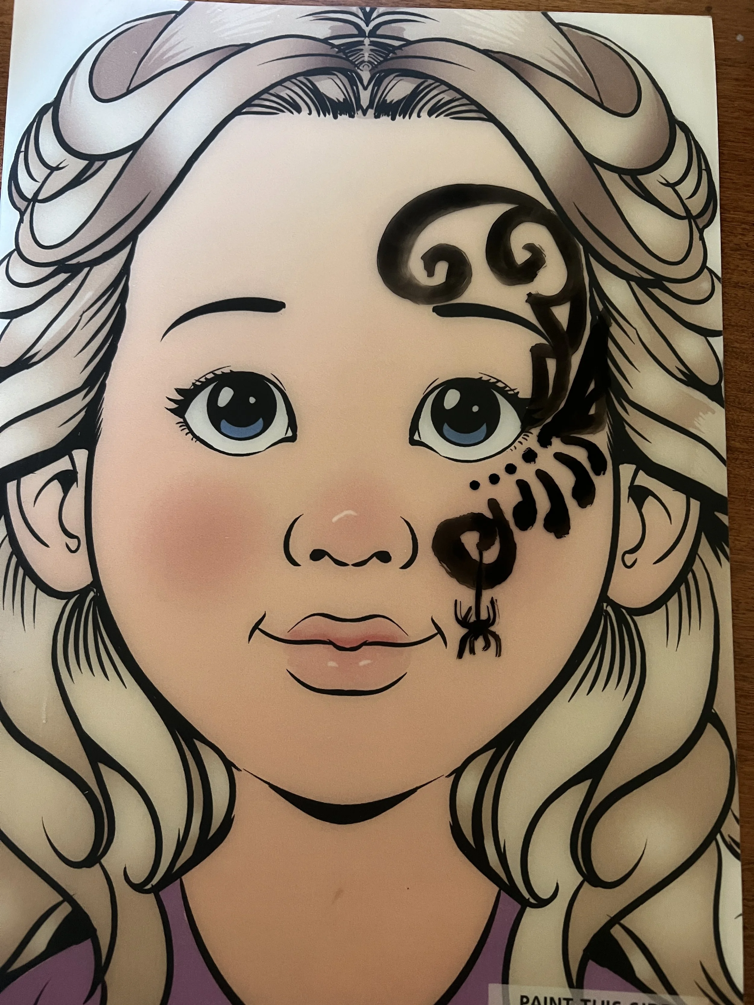 A cartoon girl with long, wavy blonde hair and big blue eyes, with a black spider on her face.