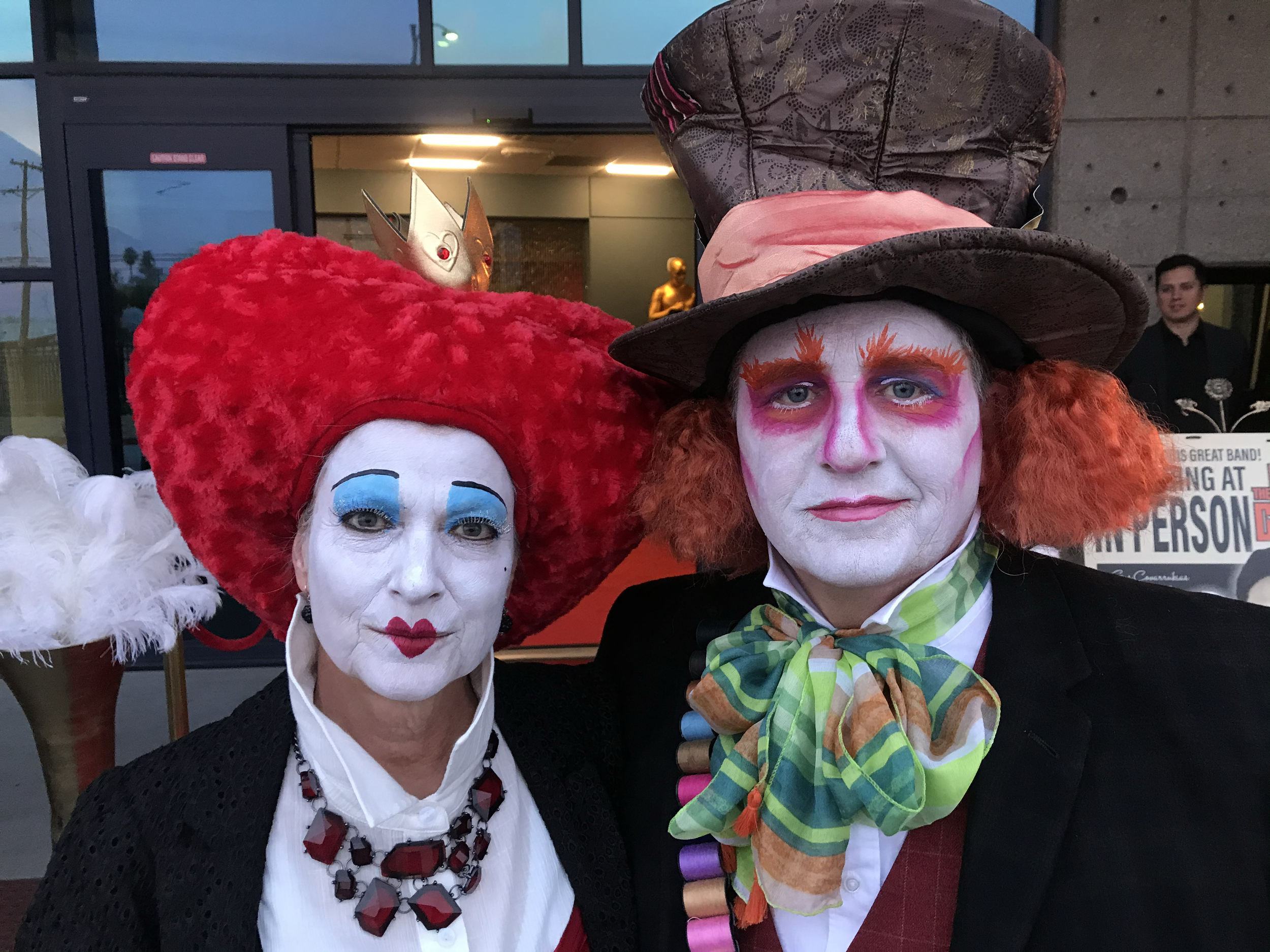 Two people dressed as the Mad Hatter and the Queen of Hearts from Alice in Wonderland with colorful makeup and costumes at a costume event.