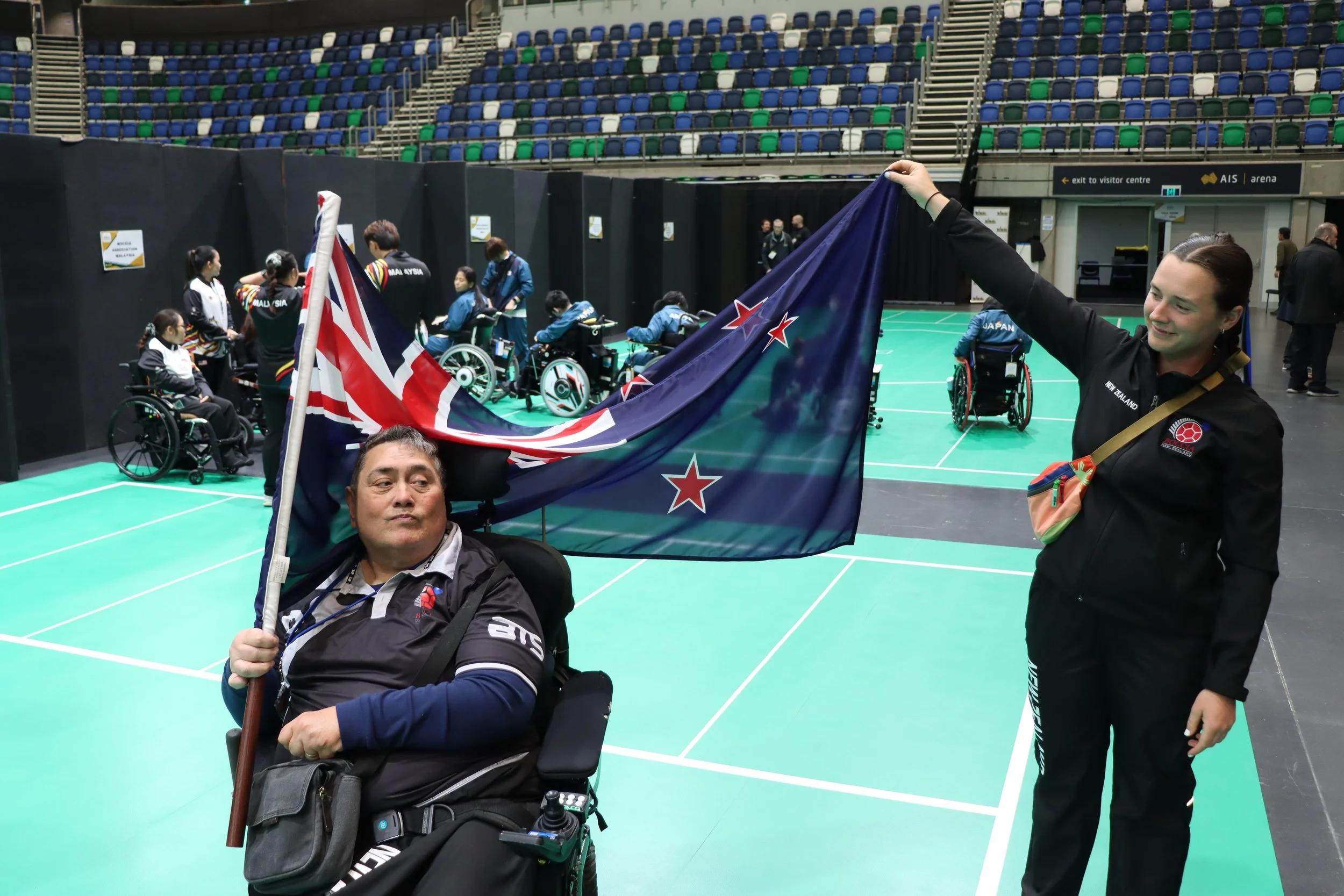 Matt Whiting and a woman hold up the New Zealand flag at a boccia tournament.