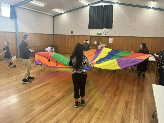 Group in gym space playing with colourful parachute
