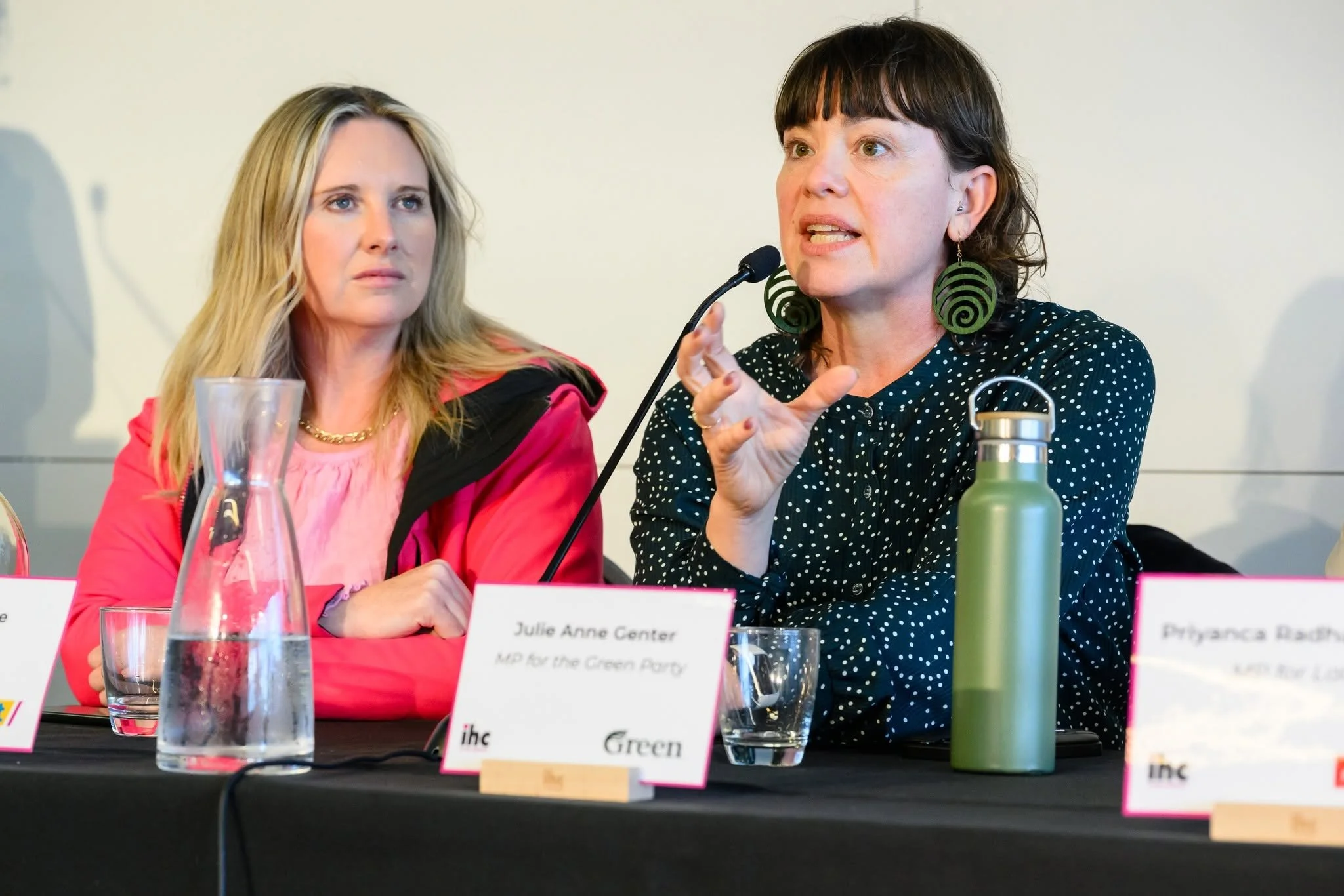Laura McClure and Julie Anne Genter at the forum table. Laura looks at Julie Anne who is speaking into a microphone.