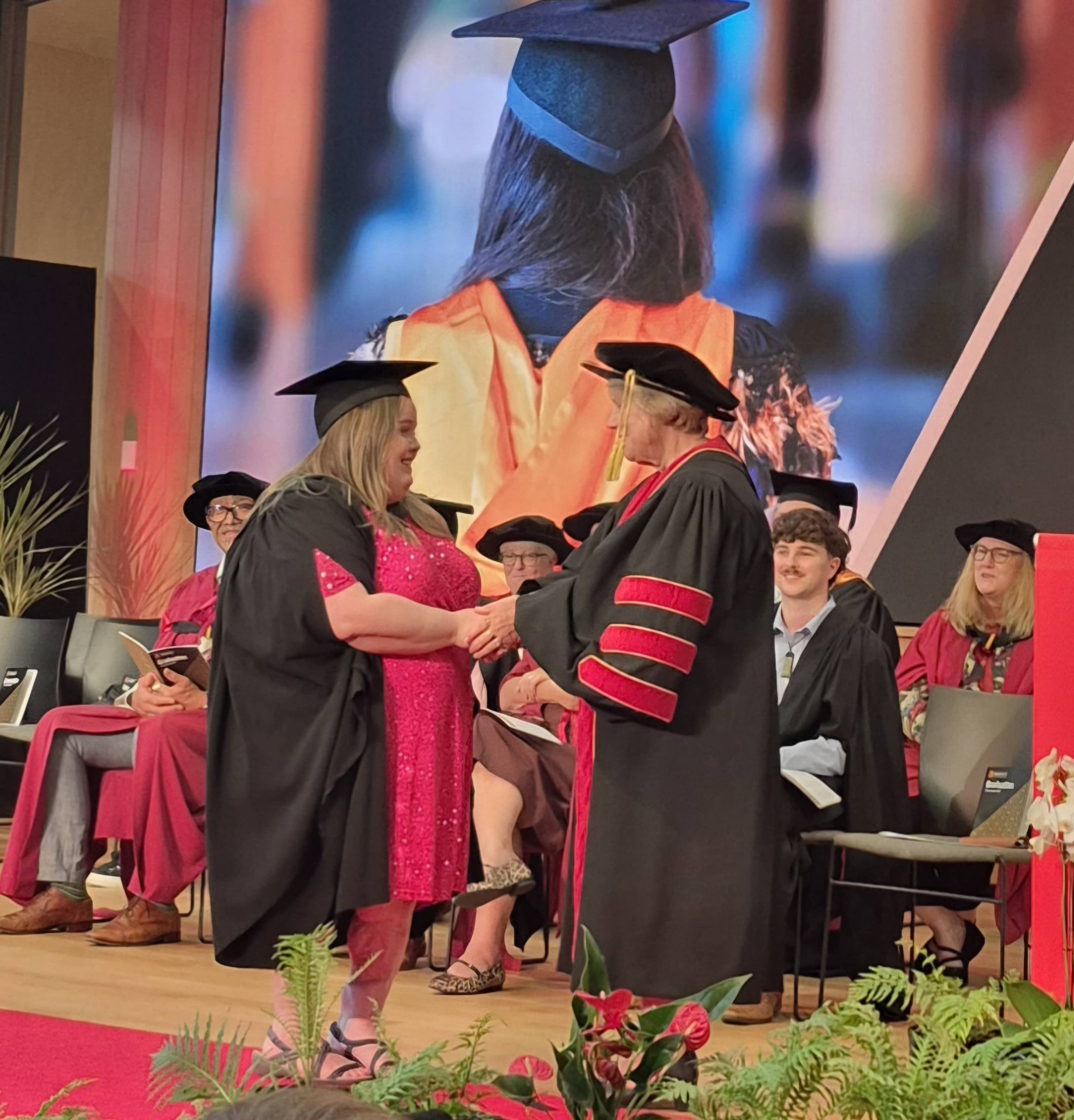 Amanda shaking professor's hand on graduation stage, both wearing ceremonial attire.