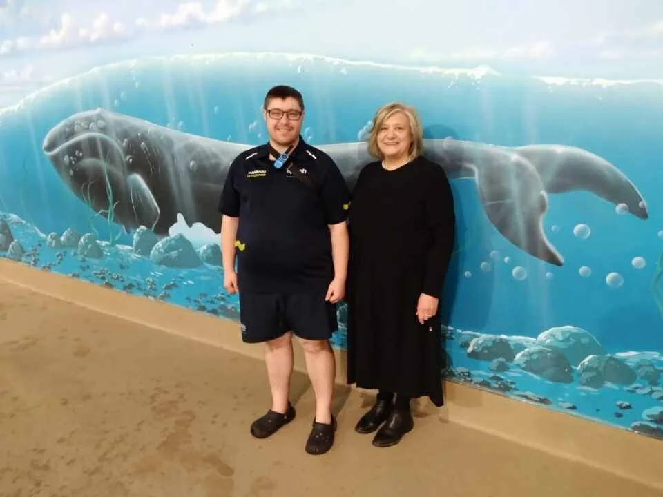 Drew and June stand smiling in front of a mural of a whale in the ocean.