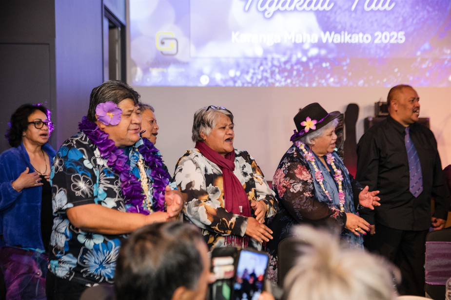 Matua and others at the ball, dressed up, in front of a projector screen.