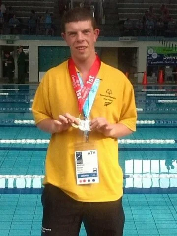 Matthew holding his gold medal at the pool.