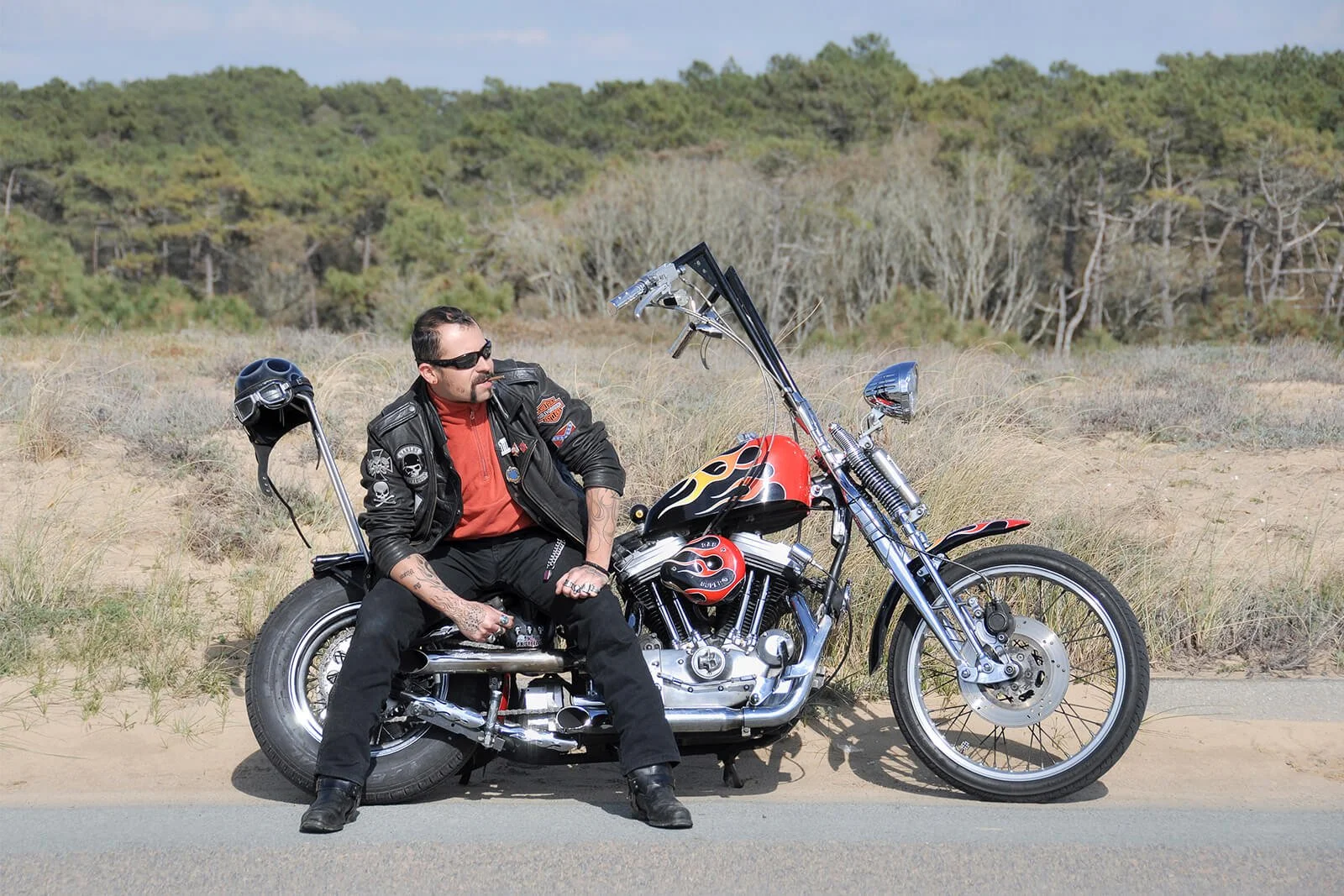 Portrait de profil d'un biker assis sur son chopper Harley Davidson le long d'une route en bordure de forêt.