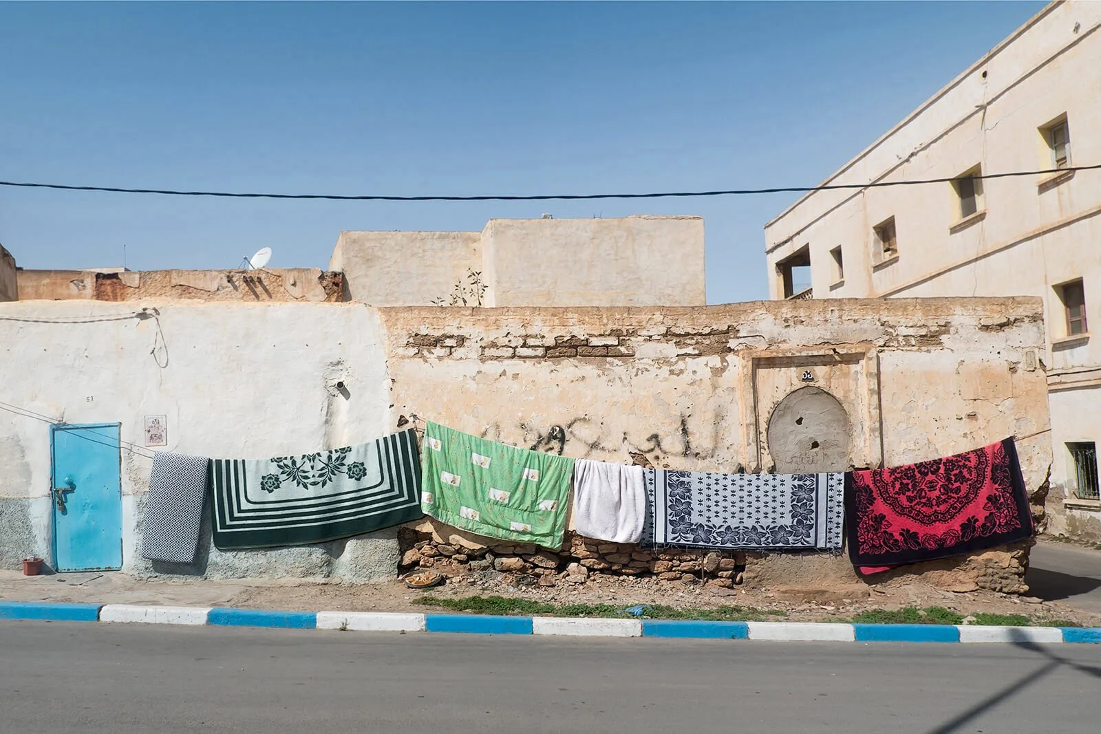 Sidi Ifni, Maroc — des couvertures sèchent sur un fil devant une façade au soleil.