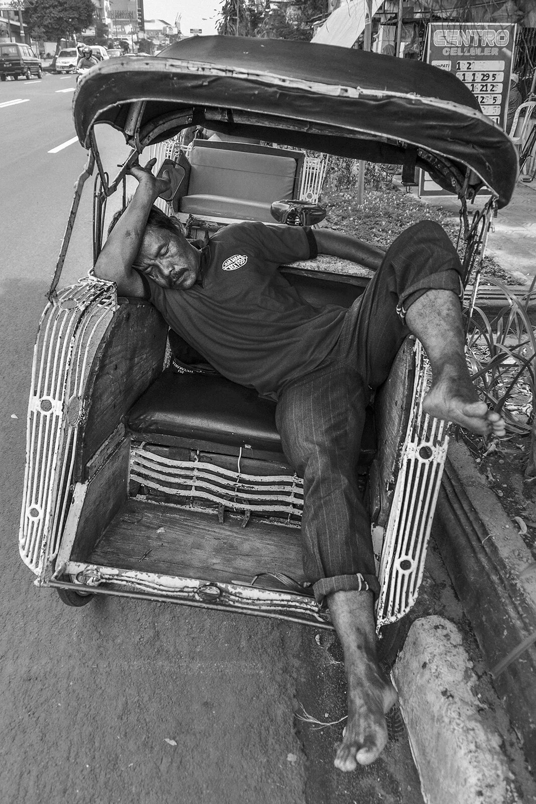 Street photography noir et blanc à Yogyakarta : un conducteur de rickshaw endormi dans son véhicule. Portrait environnemental contrasté, photo Hugues Hardy.