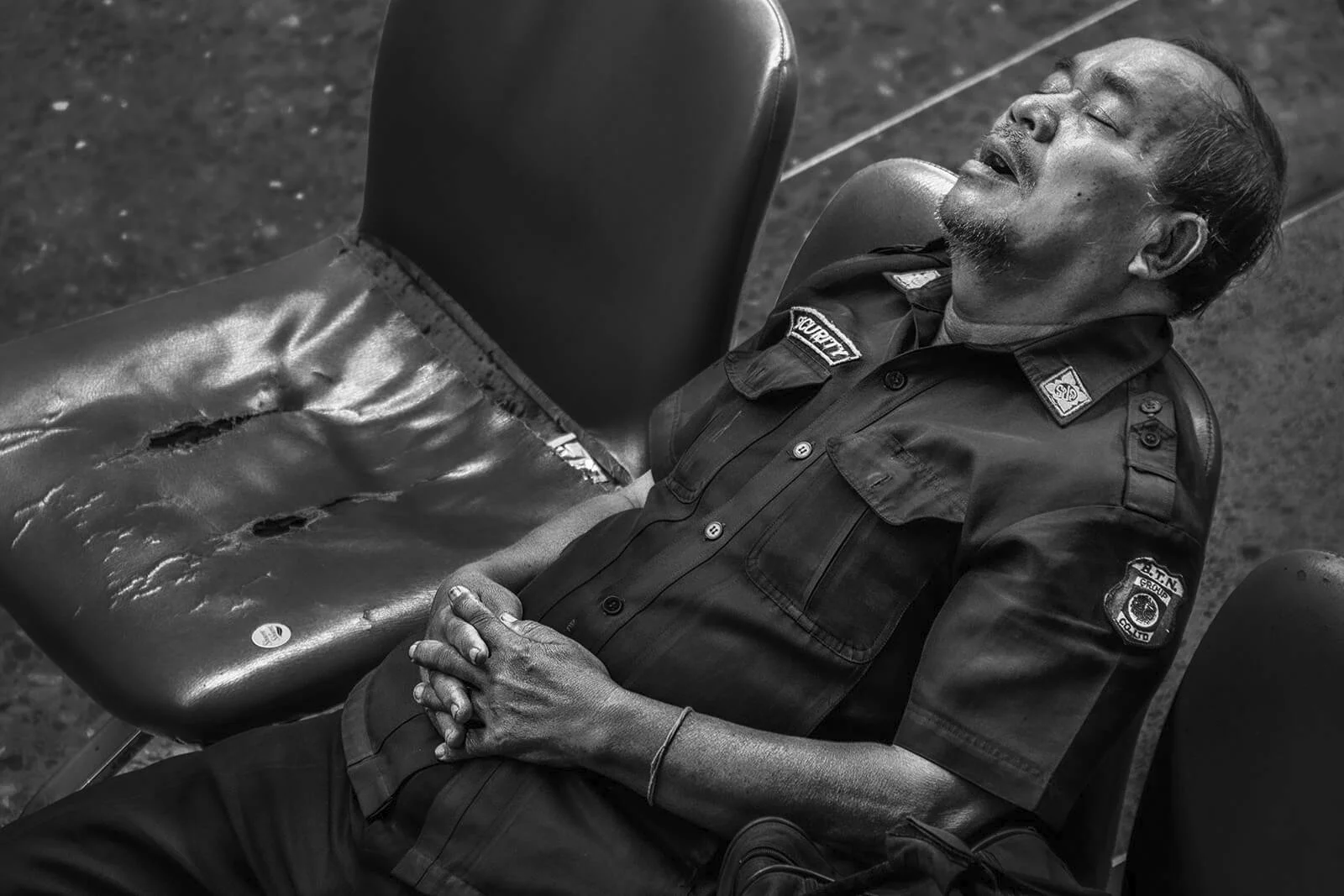 Scène de vie à Bangkok : un agent de sécurité endormi dans le hall de la gare, noir et blanc dense et contrasté. Photo Hugues Hardy.