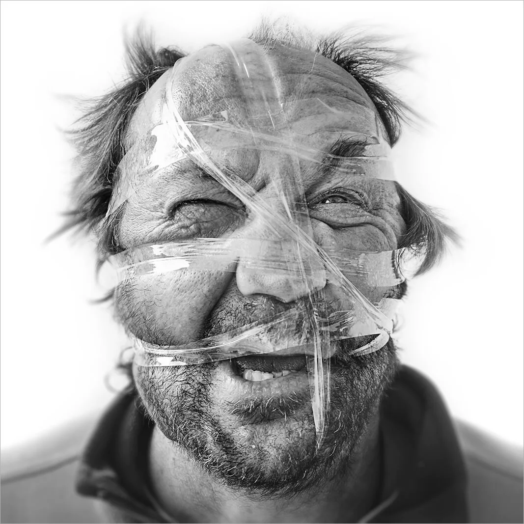 Gros plan sur un visage d'homme âgé dont les traits sont totalement compressés par le scotch adhésif. Photographie noir et blanc capturant la tension musculaire et l'effort.