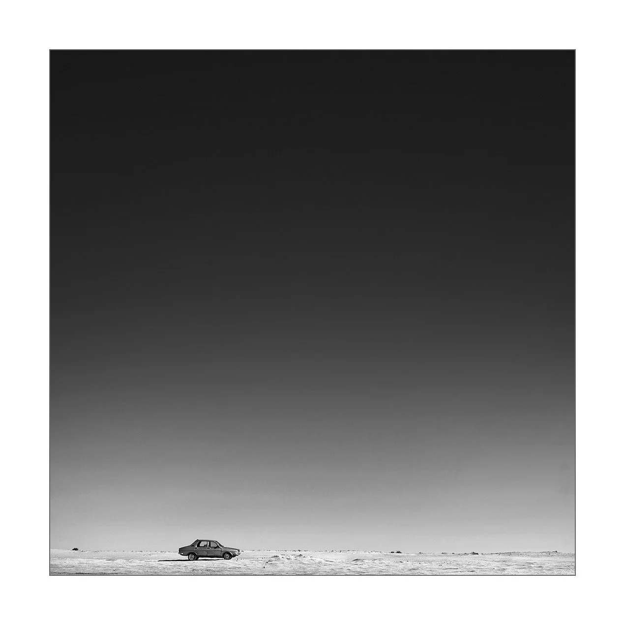 Aglou, Maroc — une Renault 12 traverse une étendue de sable sous un ciel sans nuage.