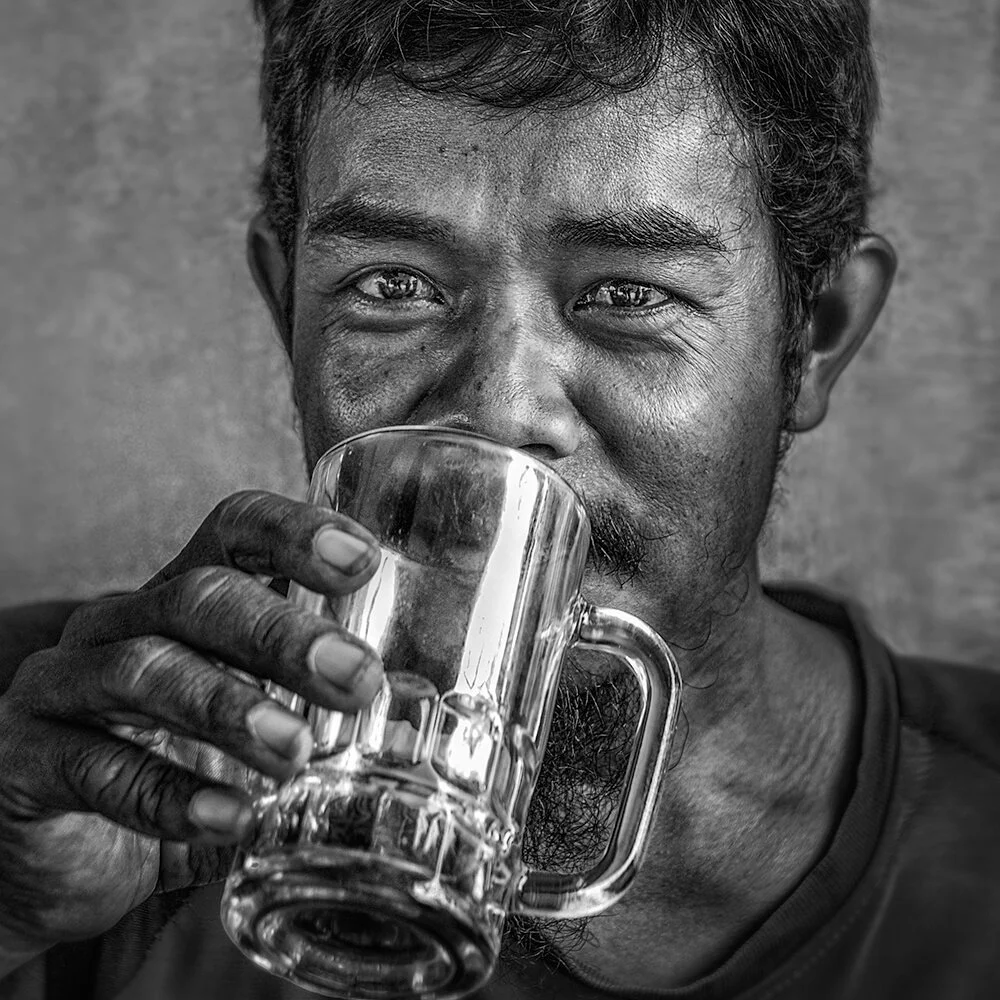 Yogyakarta, Indonésie — le regard direct d'un jeune homme qui boit un grand verre de thé.