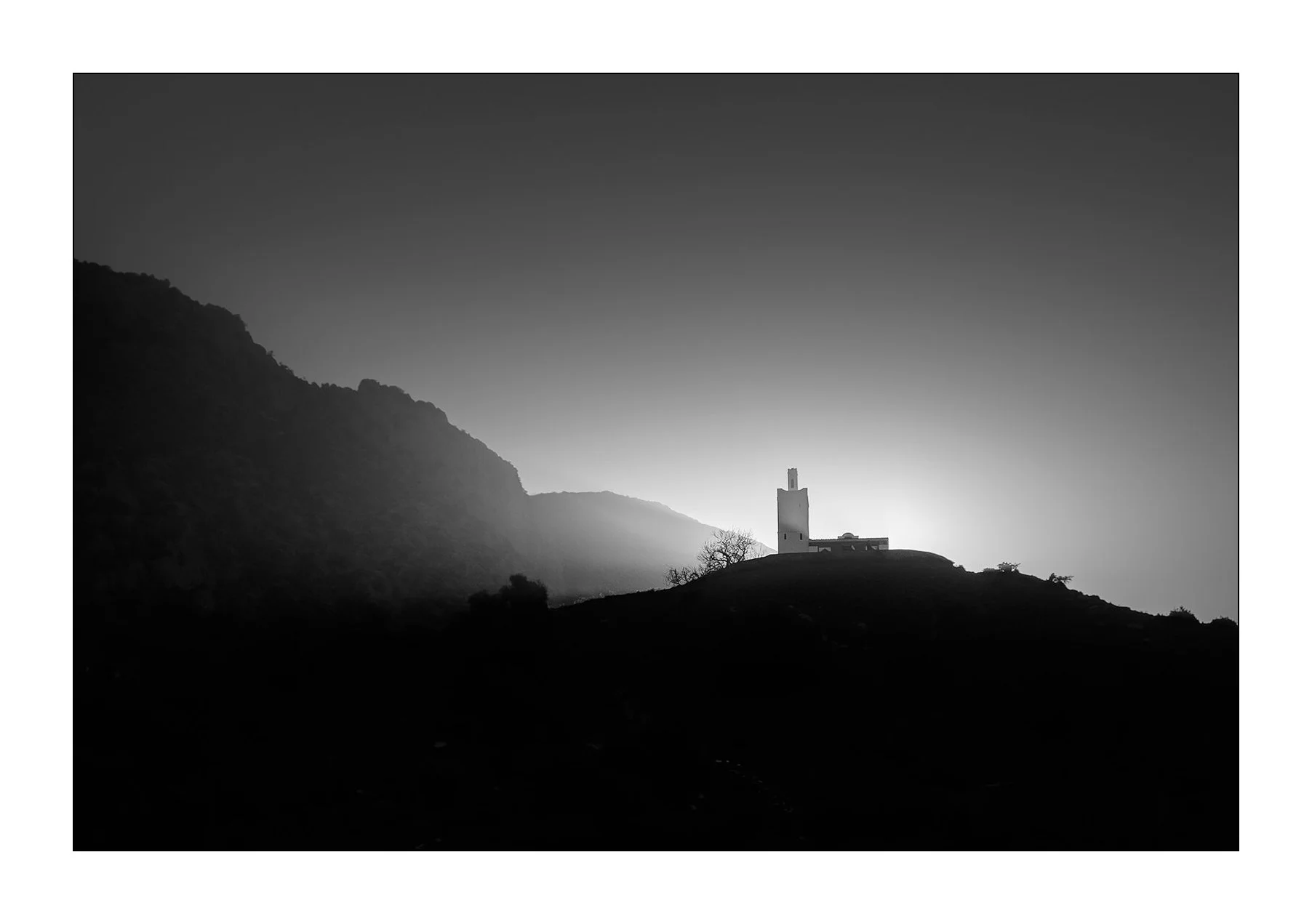 Chefchaouen, Maroc — la silhouette d’une mosquée et de quelques arbustes se détache sur une colline au lever du jour.