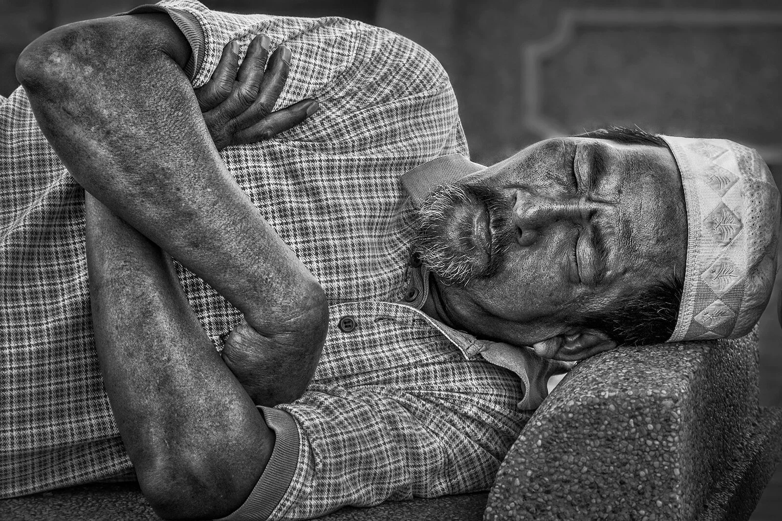 Street photography noir et blanc dense : un homme utilise une bordure en béton comme oreiller à Penang en Malaisie. Style contrasté.