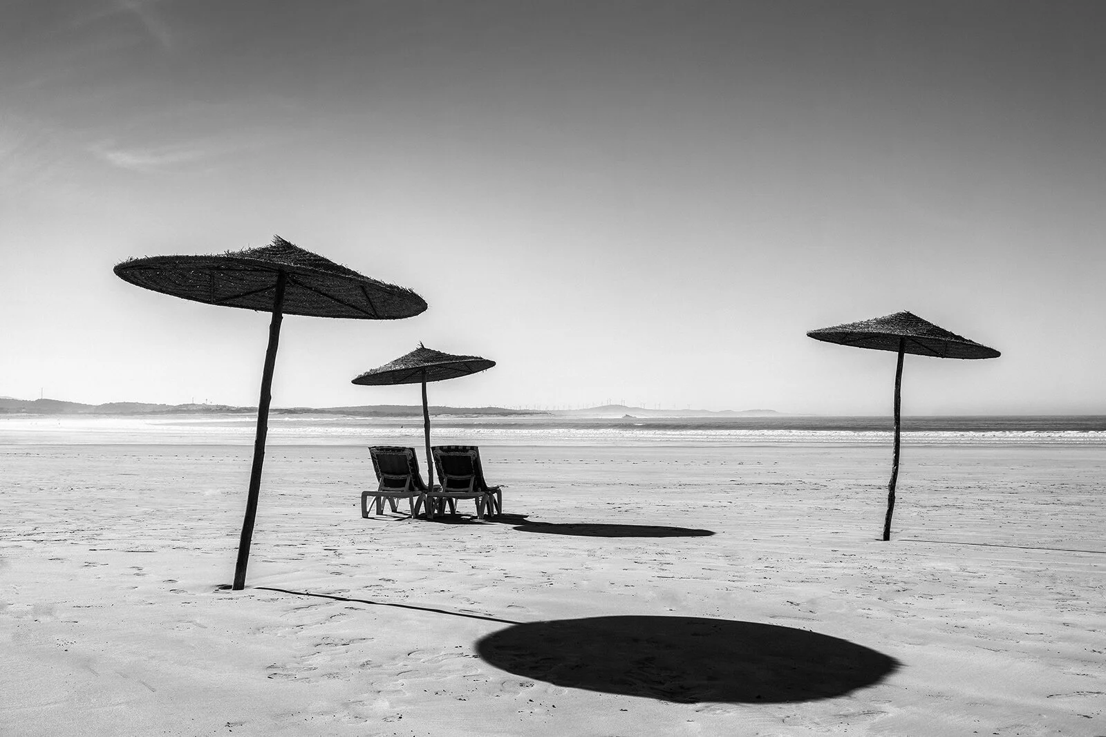 Scène de plage à Essaouira. Géométrie d'ombres portées par des parasols et chaises vides, style noir et blanc contrasté et graphique.