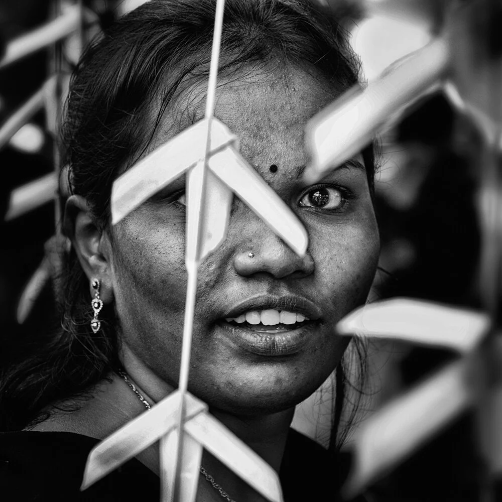 Batu Caves, Malaisie — le visage d’une jeune femme apparaît derrière des guirlandes de papier.
