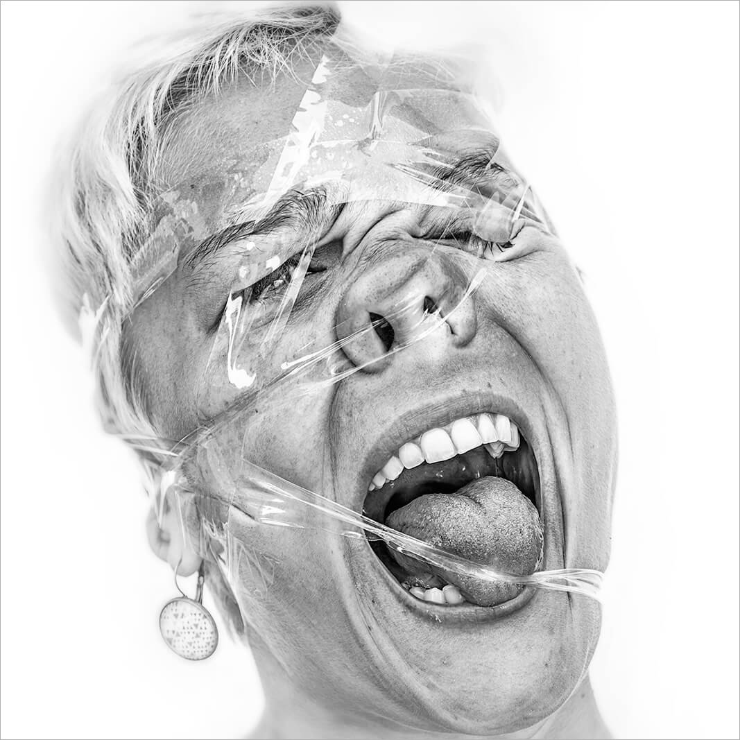 Expression faciale intense d'une femme tentant de briser l'adhérence du scotch par la seule force des muscles du visage. Portrait noir et blanc original et décalé.