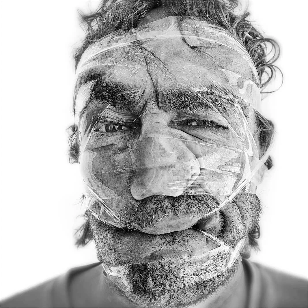 Focus sur un visage déformé par plusieurs bandes de scotch, accentuant les plis du front et l'effort des muscles zygomatiques. Une étude humoristique de la physionomie humaine.