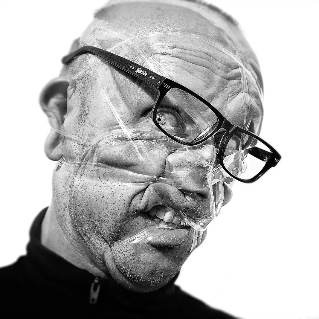 Gros plan sur un visage masculin dont la bouche est tirée par le scotch, créant une expression hilarante de résistance musculaire. Photographie de portrait conceptuelle et drôle.