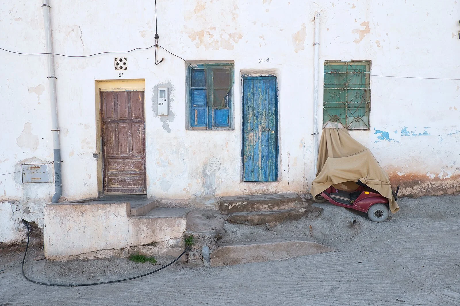 Sidi Ifni, Maroc — un fauteuil roulant électrique est stationné dans la rue devant une rangée de portes colorées.