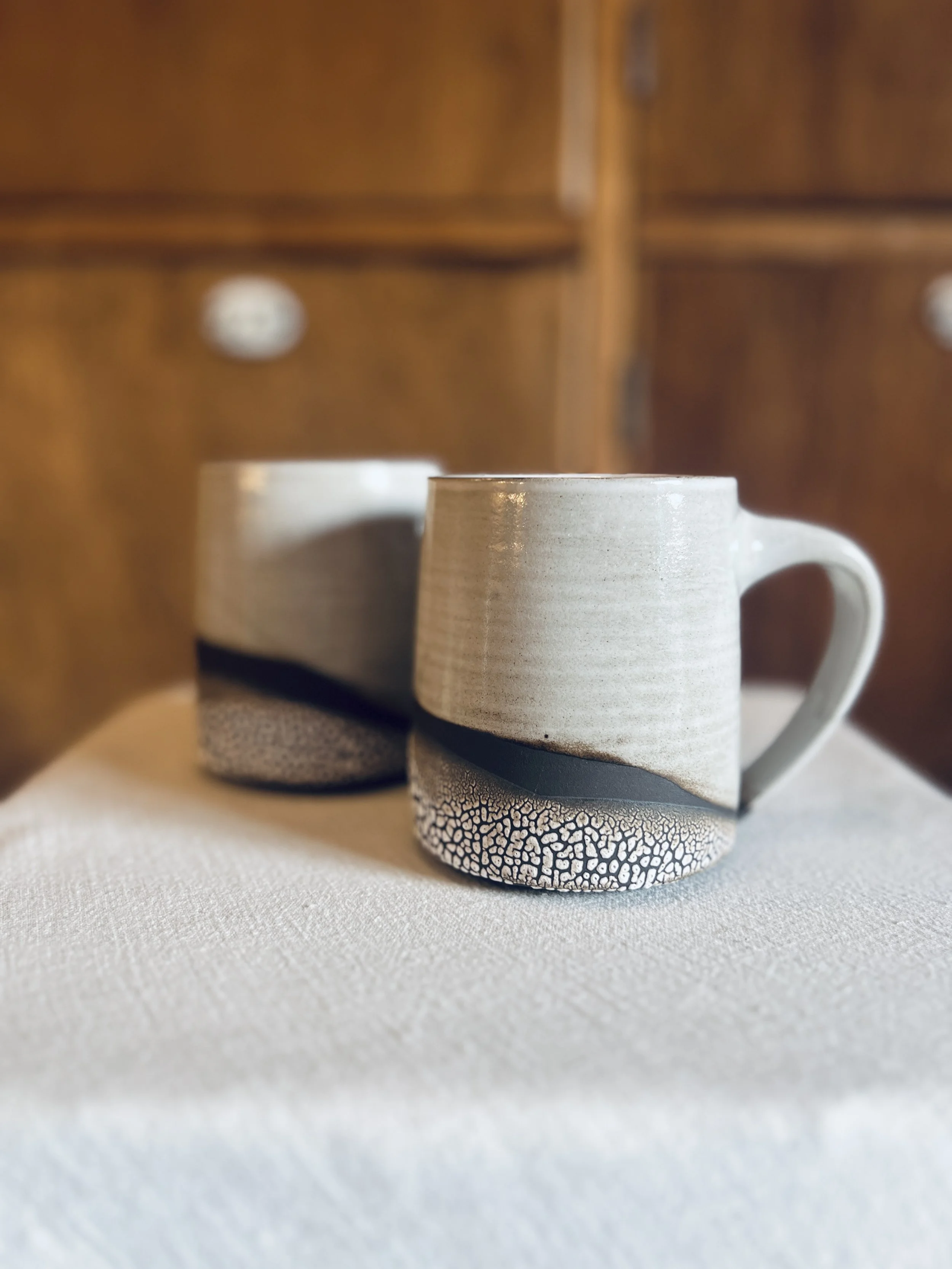 Close-up of a ceramic mug with textured bottom sitting on a white surface, with a wooden cabinet in the background.