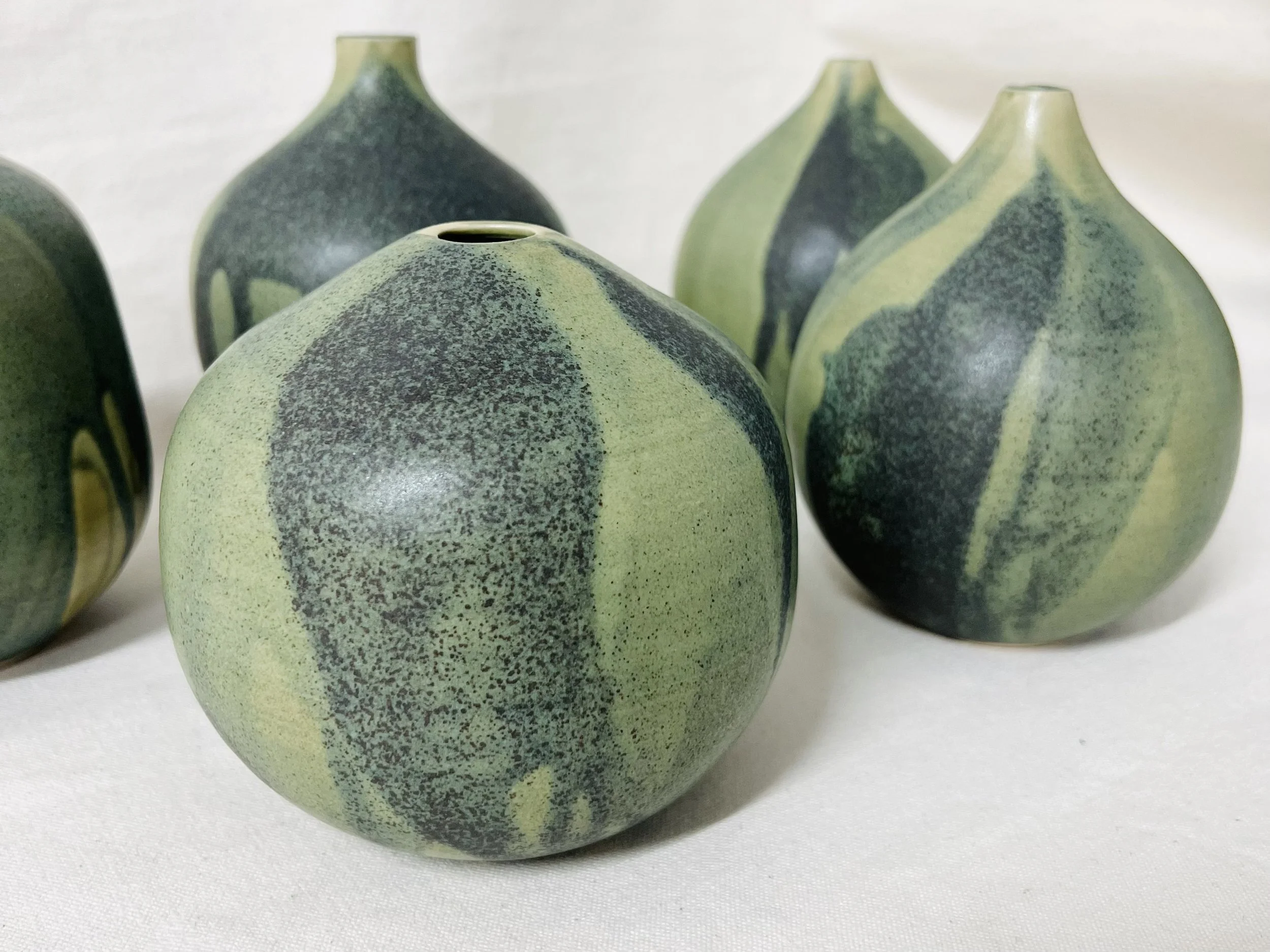 Multiple green and black ceramic vases with speckled and striped patterns on a white surface.