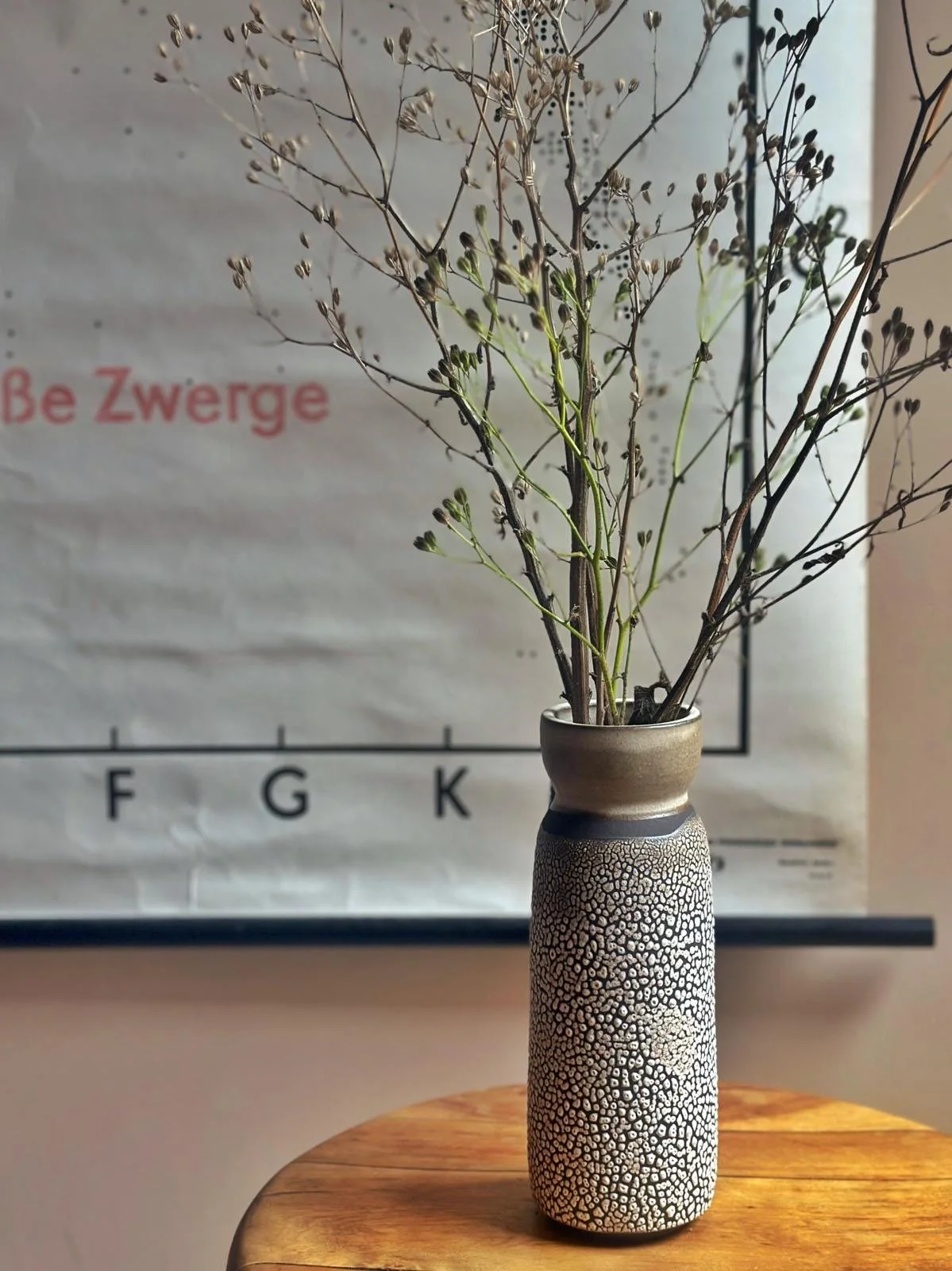 Handmade textured ceramic vase by Kim Plimley displayed with dried foliage at home