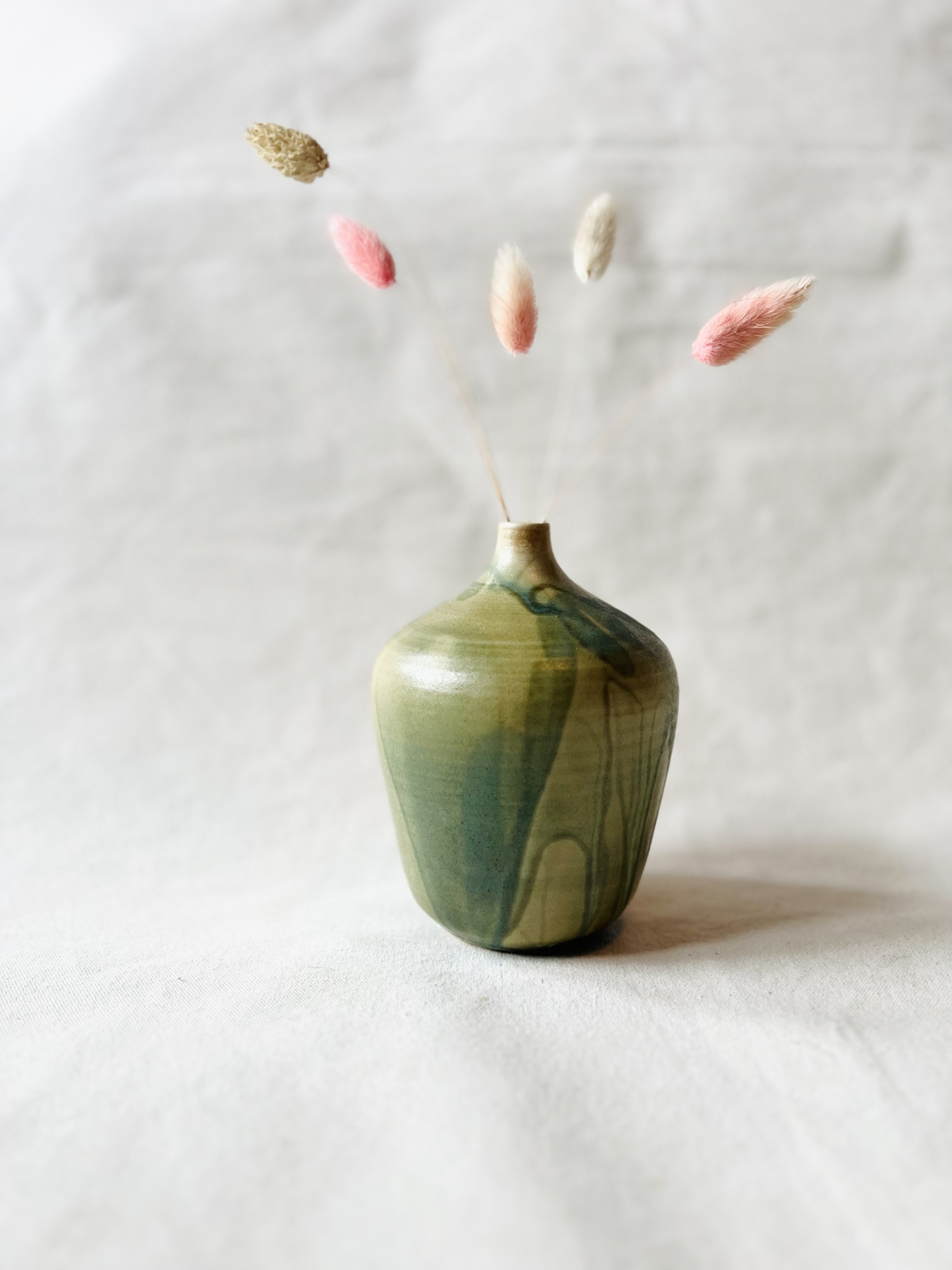 A ceramic vase with a green and beige swirl pattern holding five dried flowers with fuzzy pink and beige buds, arranged against a plain white background.