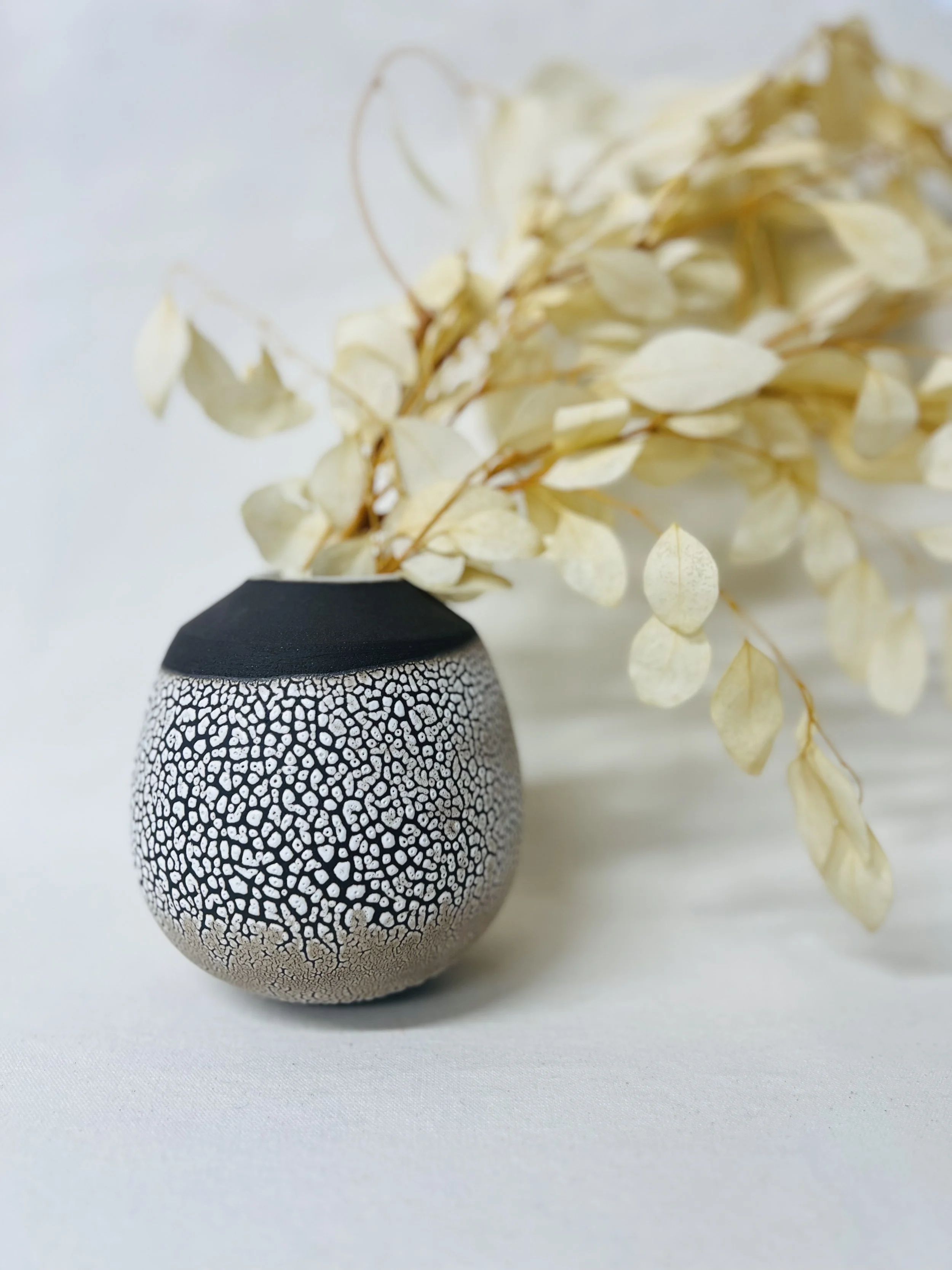 Black and white patterned ceramic vase with dried white leaves arranged inside.