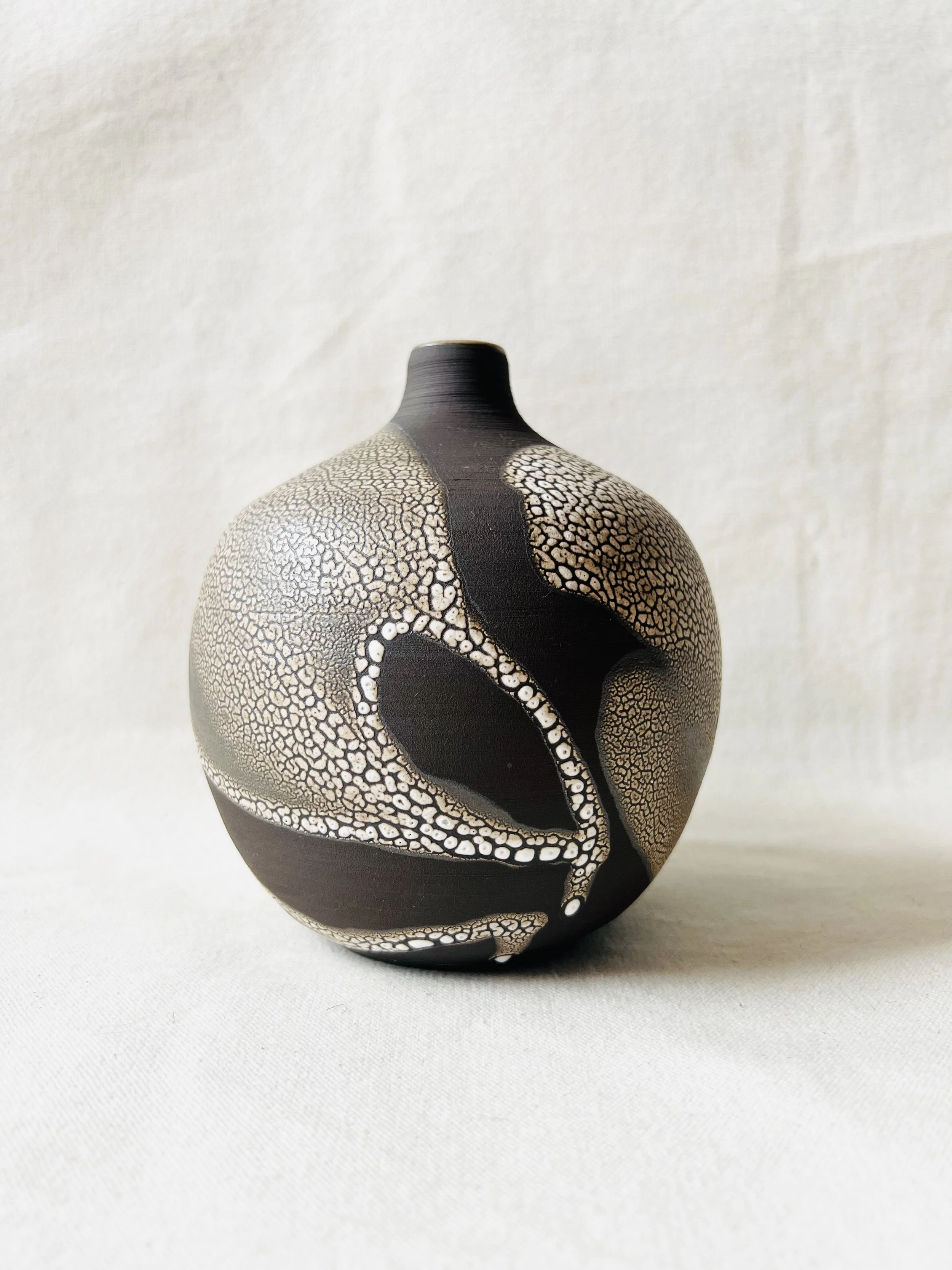A decorative ceramic vase with black and white cracked pattern and textured design, placed on a white fabric surface.