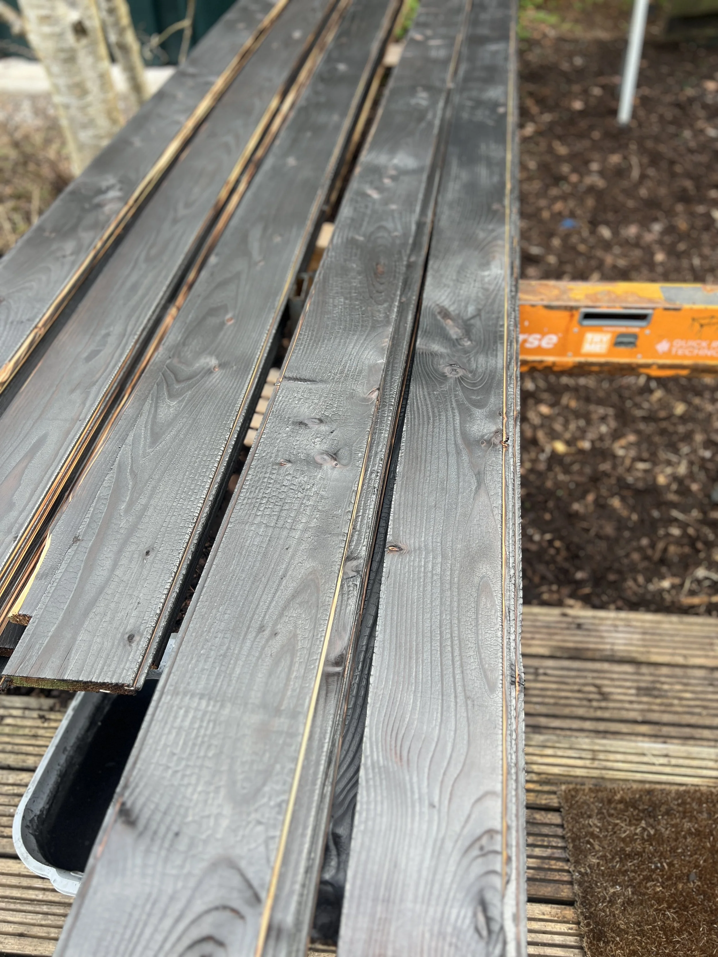Timber boards being hand burned to create black cladding for the pottery studio exterior