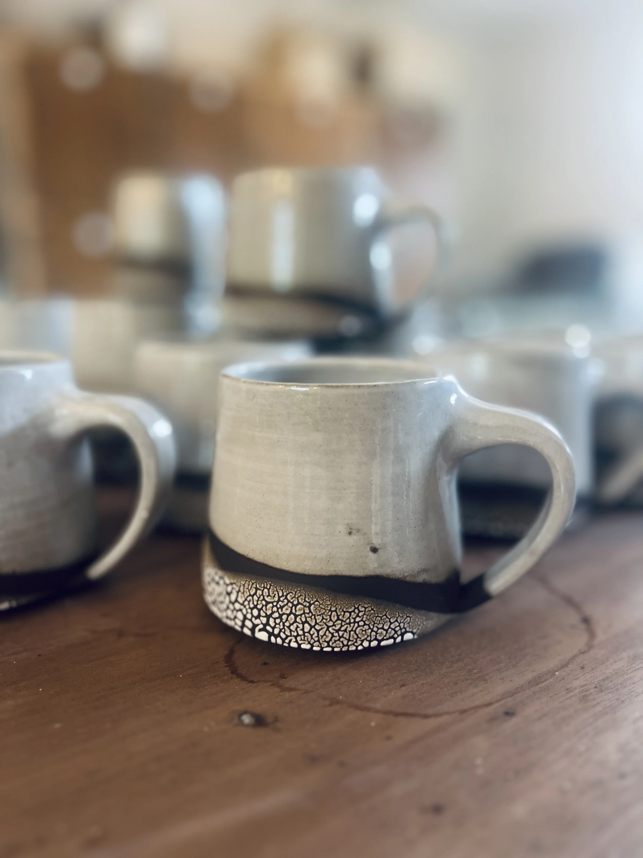 Close-up of several beige ceramic coffee mugs placed upside down on a wooden surface, with a blurred background.