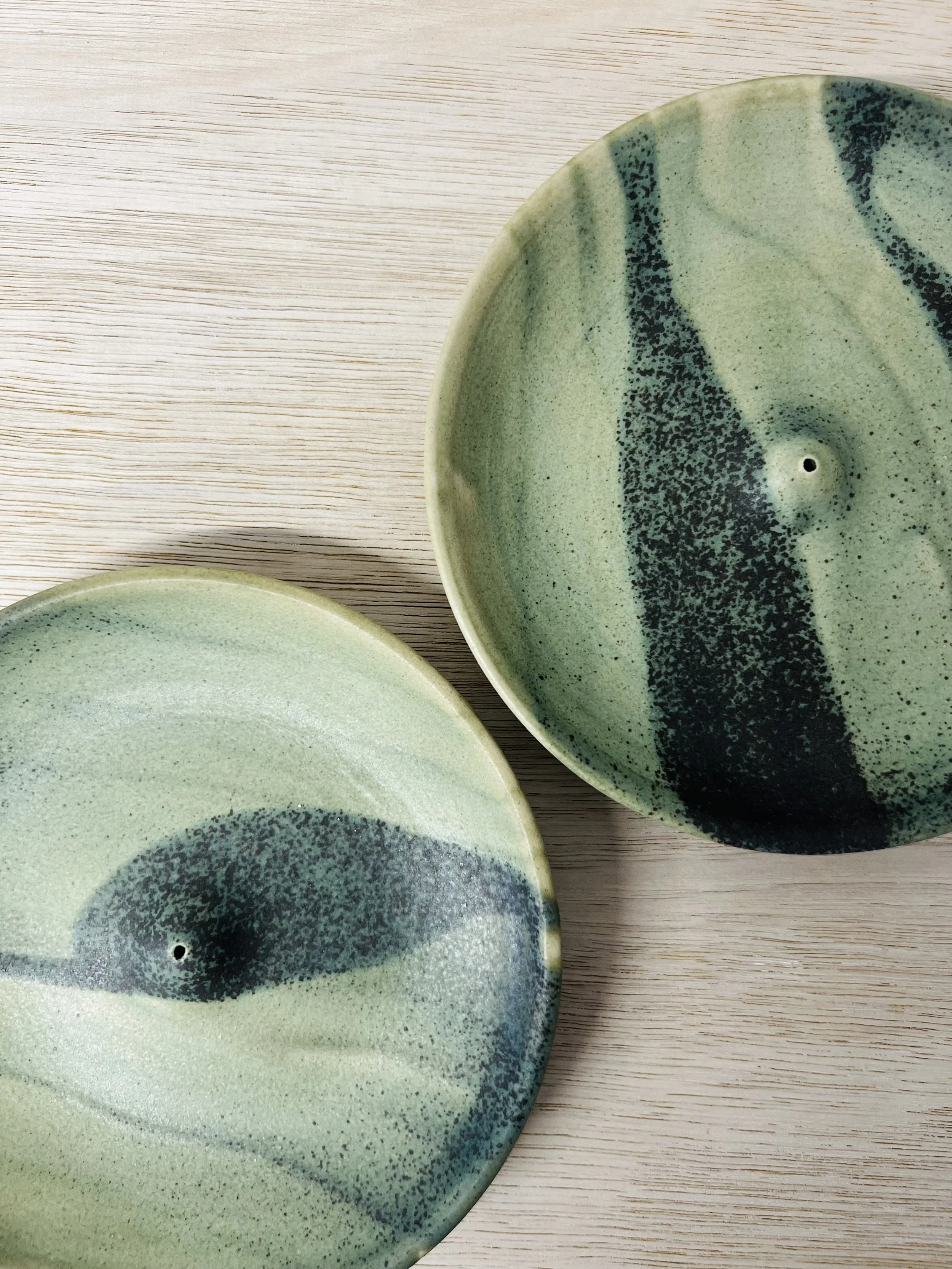 Two ceramic bowls with a green glaze and dark speckled pattern on a light wooden surface.