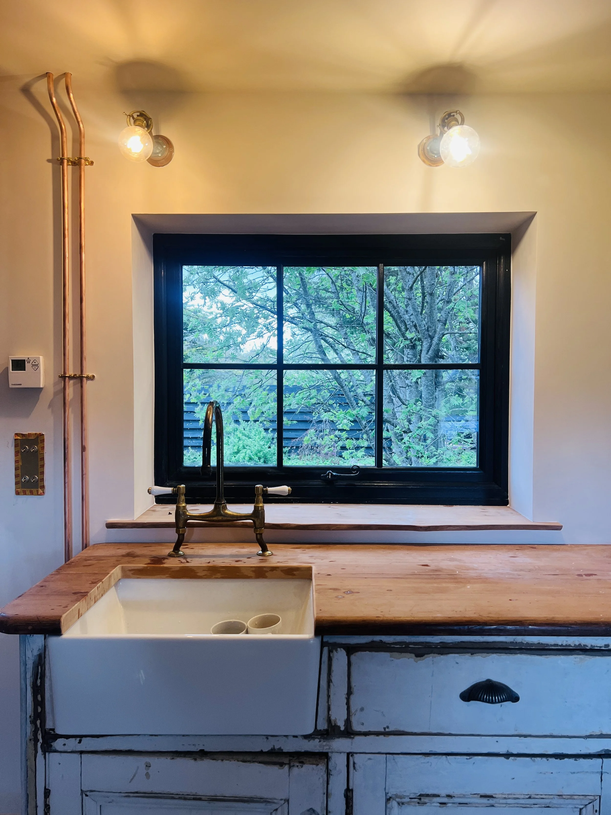 Salvaged wooden workbench with ceramic sink beneath a window in a pottery studio