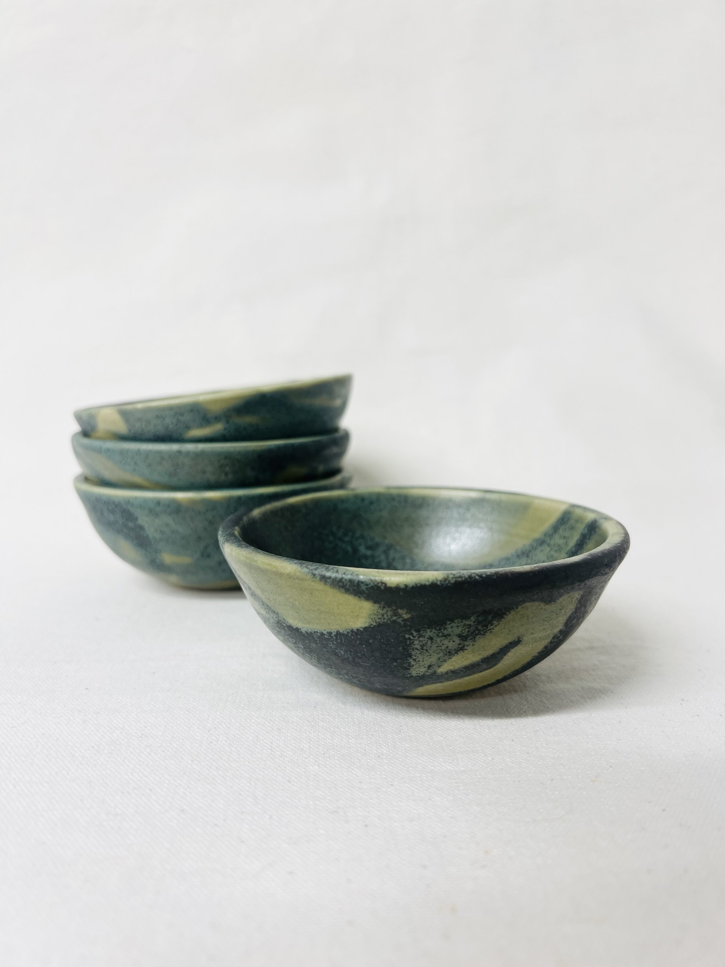 Four small ceramic bowls with a blue and yellow marbled glaze, stacked in a slightly staggered arrangement on a white background.