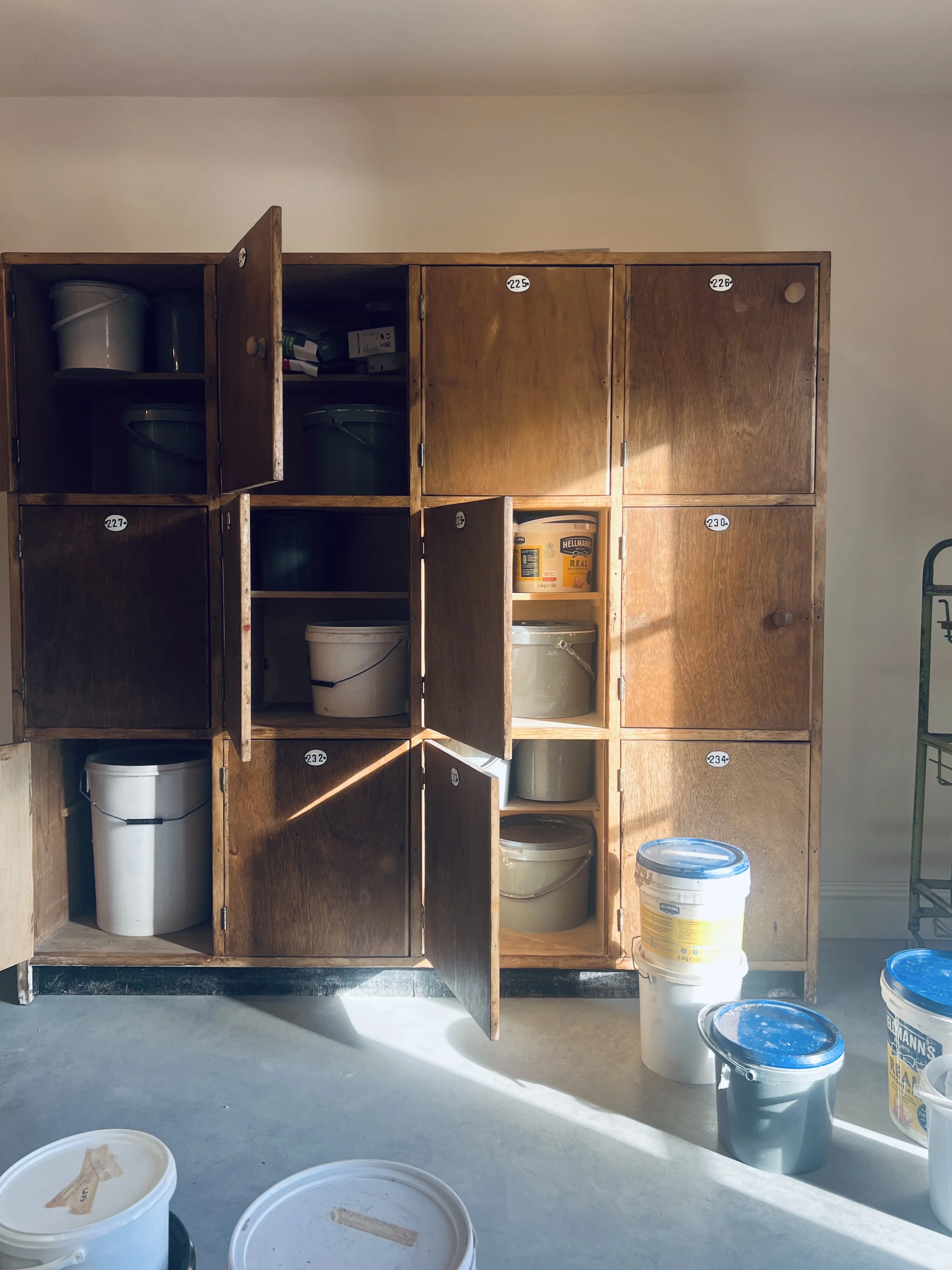 Clay, slip and glaze tubs stored inside vintage wooden lockers in a working pottery studio