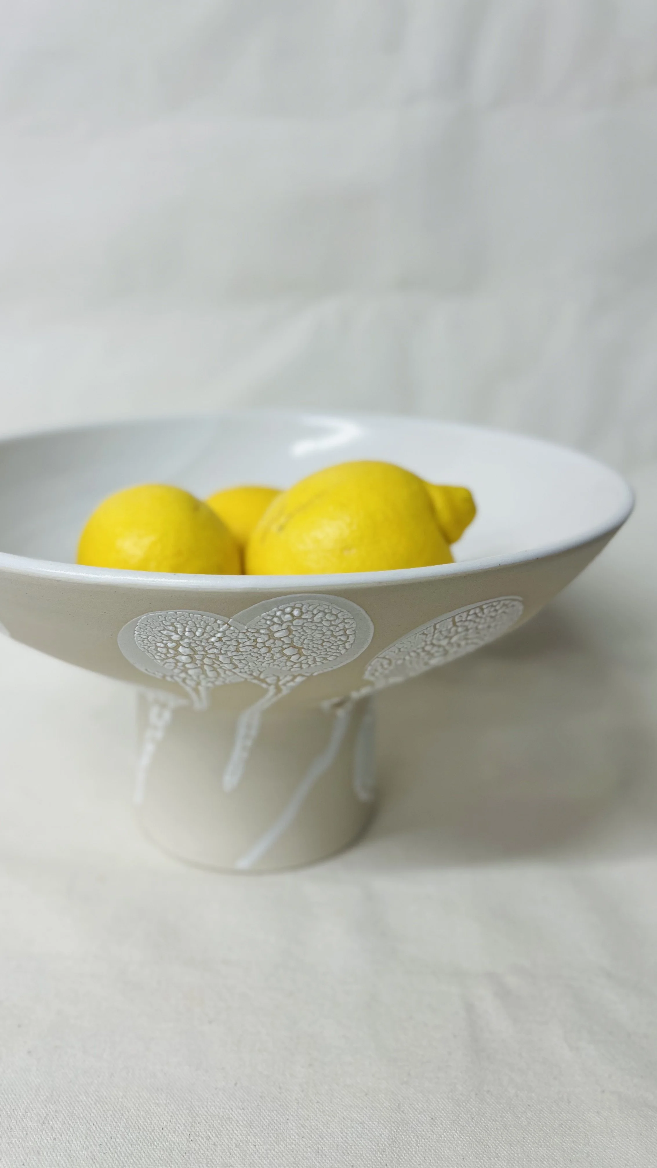White bowl with a decorative heart pattern, holding three yellow lemons on a white surface.
