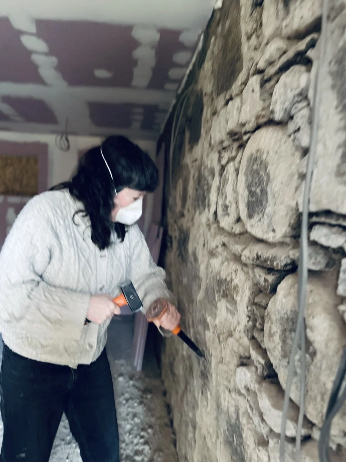 Kim Plimley removing old mortar by hand to reveal the original granite wall in her Carrbridge pottery studio