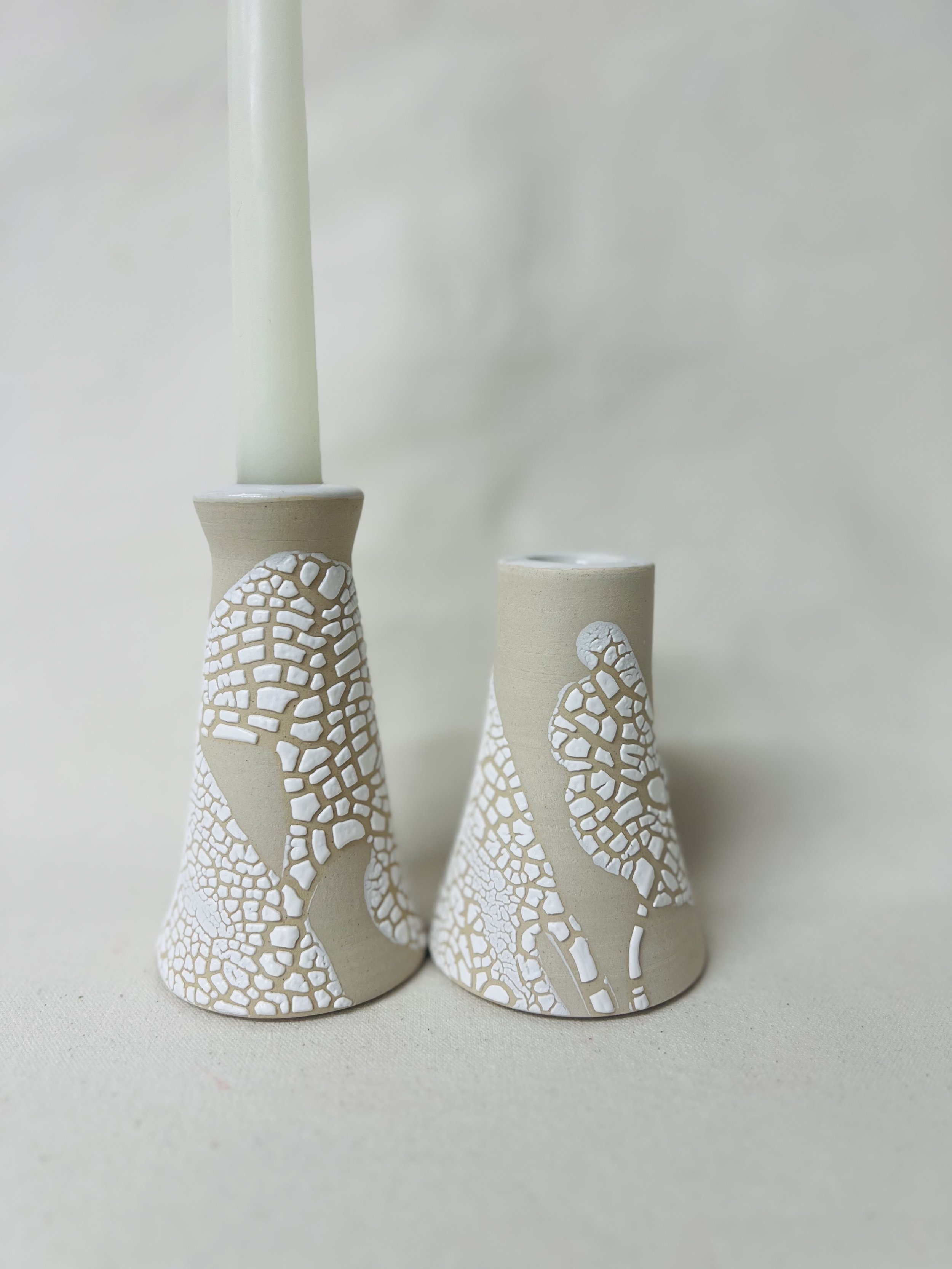 Three beige ceramic vases of varying heights with white textured mosaic patterns around their bases and lower sections, set against a plain, light-colored background.