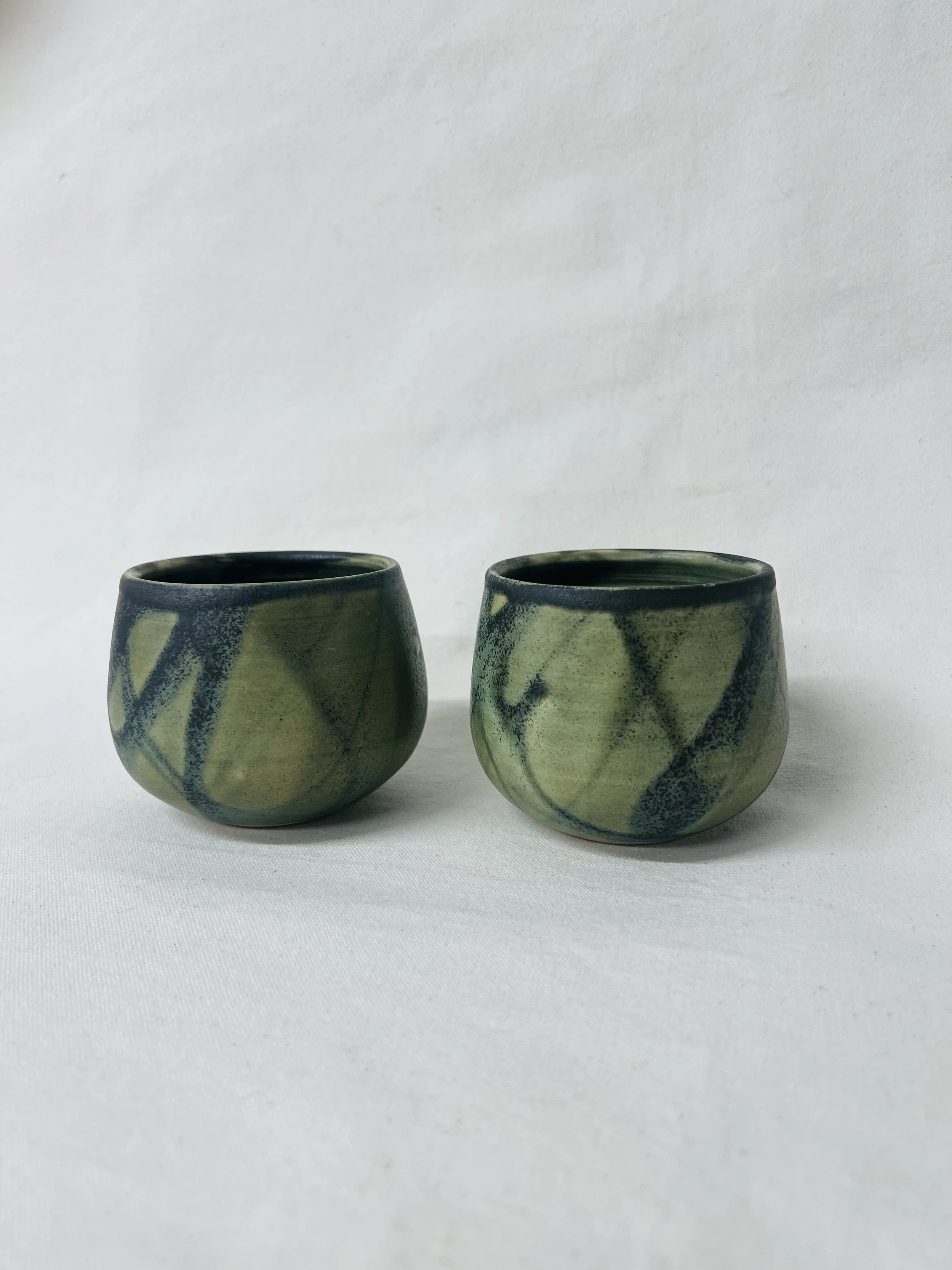 Two ceramic cups with green and black abstract patterns on a white background.