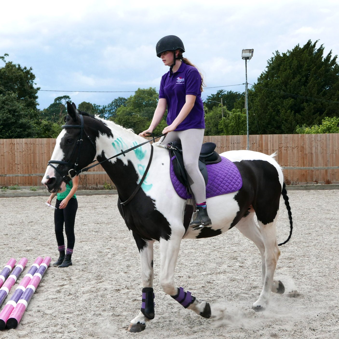 A young girl riding a brown and white horse with minder watching over her, wearing Foxglove Farm polo t-shirts in signature purple with logo designed by Yeswaydesign