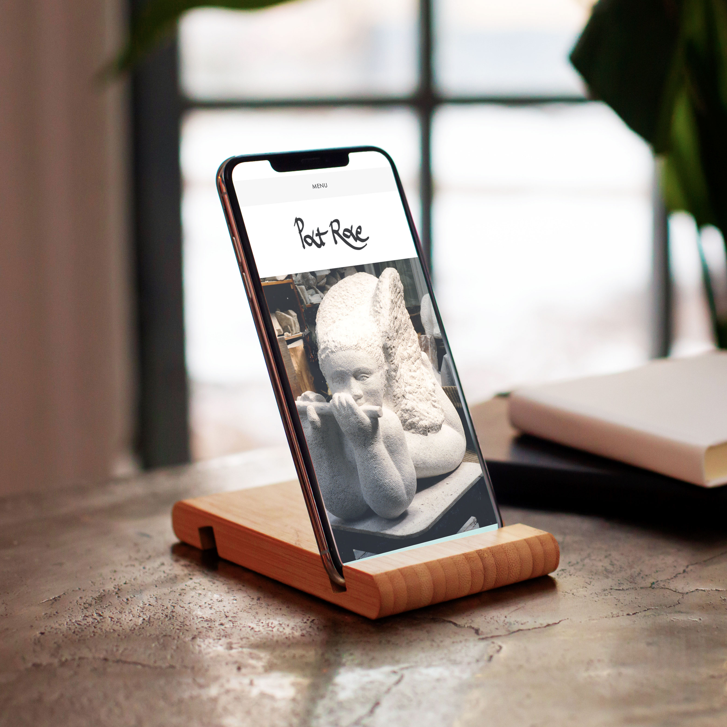 iPhone on a table showing artist and sculptor Pat Rae's logo and website with a window and plant in background designed by Yeswaydesign