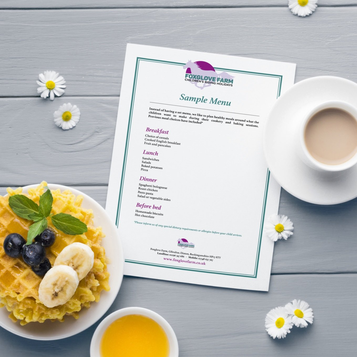 Foxglove Farm Menu designed by Yeswaydesign photographed on a wooden breakfast table with daisies scattered around, a waffle on a plate, with slices of banana, blueberries, mint, coffee, orange juice