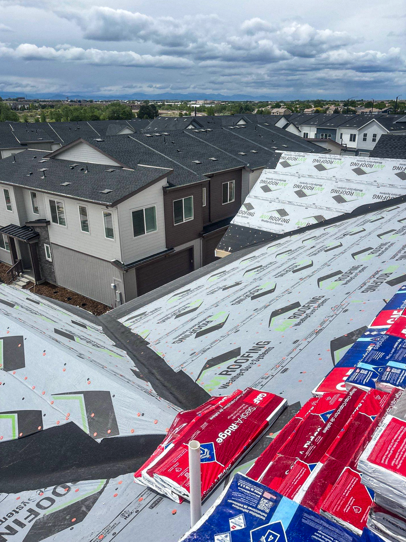 A image featuring a roofing project for a residential complex. The roof has AVI Roofing underlayment installed and GAF shingles are loaded on the roof in preparation for installation.