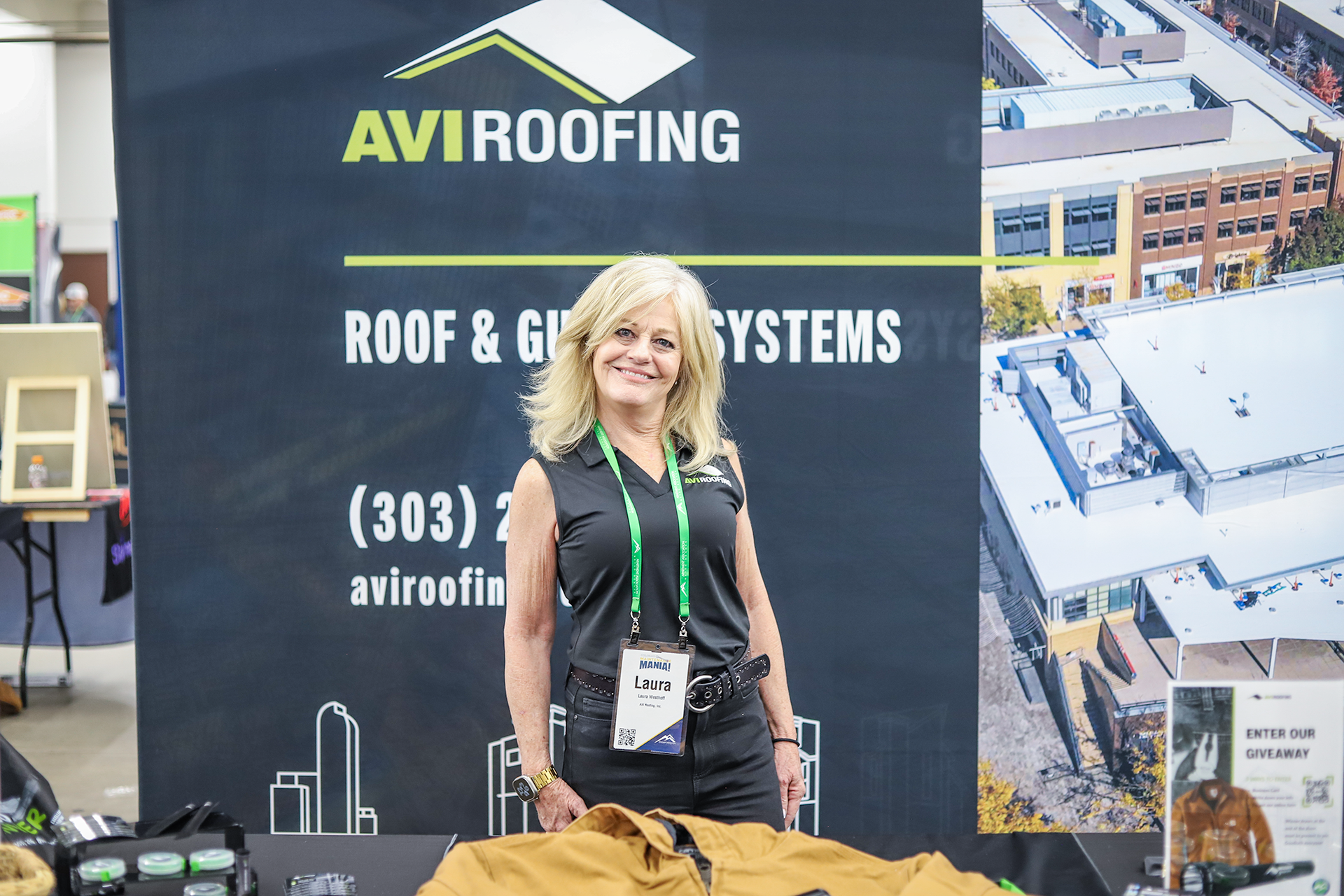 Laura Westhoff, AVI Roofing's Business Development Director smiles at the camera behind AVI's tradeshow booth.